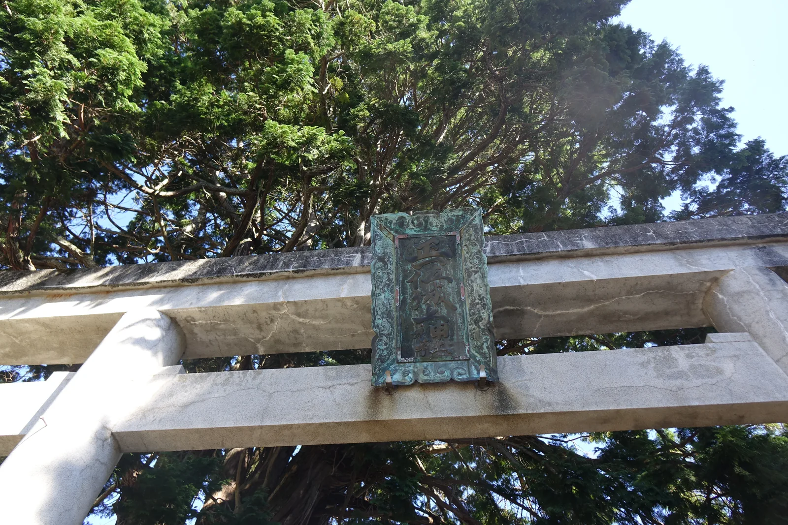 城上神社石造鳥居笠木中央的銅鑄扁額，框上滿是唐草浮雕，銅面已整片轉成青綠