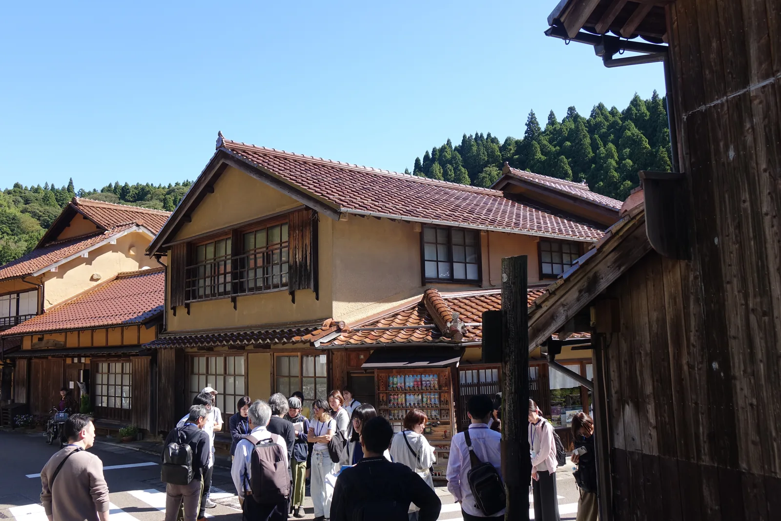 上午的大森町並み，前景是燒杉的黑色板壁，赤瓦的屋頂一排排往深處退，一團訪客站在路中間