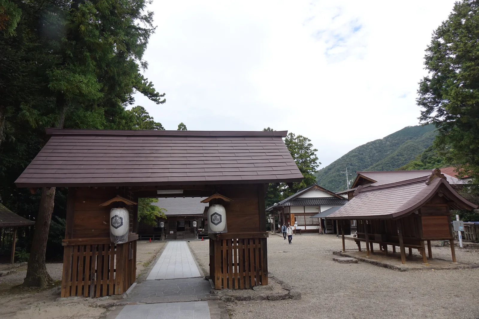 須佐神社的隨神門，八腳的門，屋頂厚實，兩根柱間各掛一盞白紙燈籠，門下石板路直通拜殿