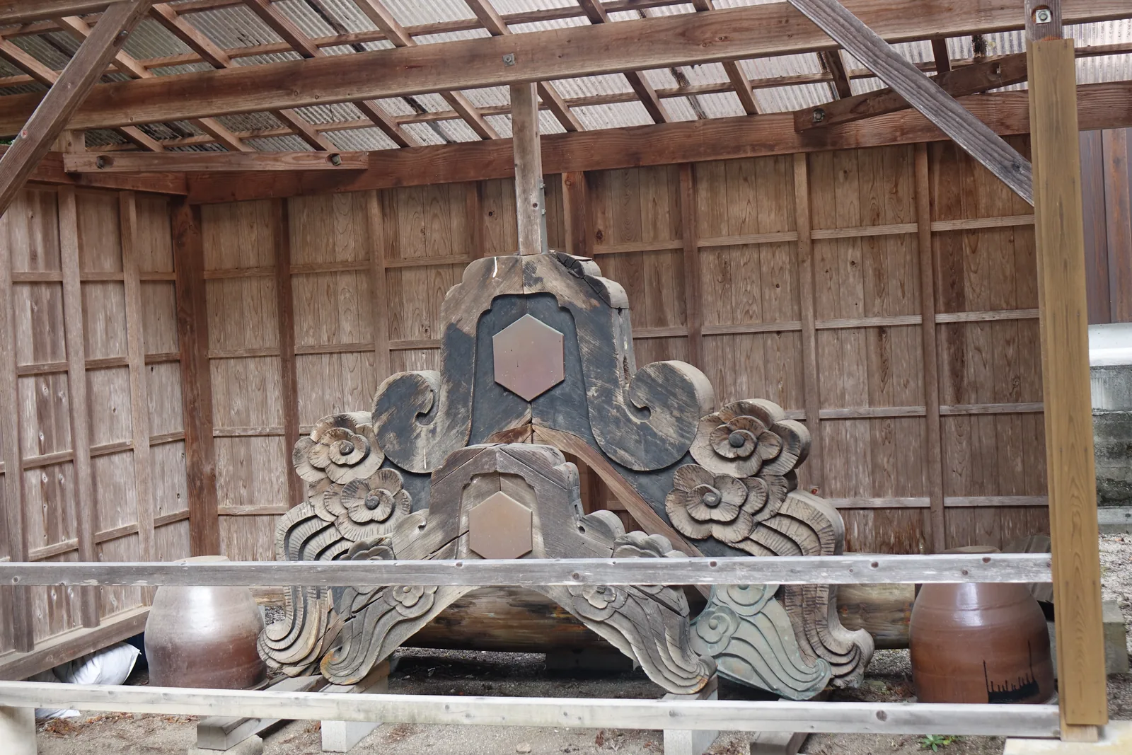 須佐神社境內棚架上擱著一對拆下來的懸魚，牡丹與雲的浮雕層層疊疊，中央嵌著六角形銅板