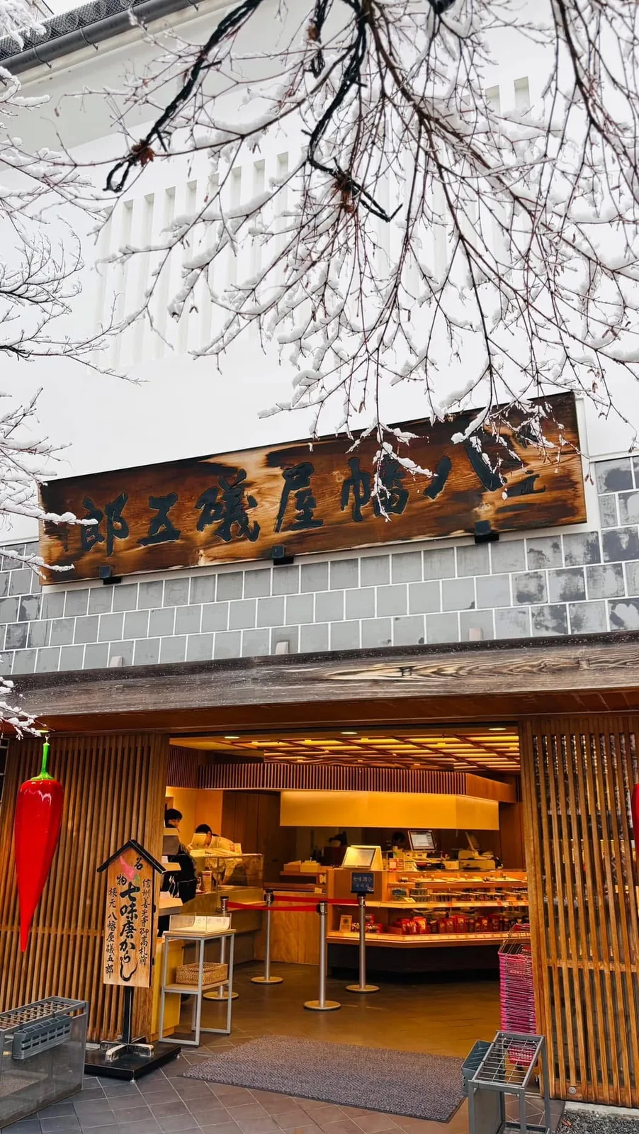 八幡屋礒五郎本店店頭，雪積在右起橫書的木製看板上，門口掛著紅色唐辛子造型的裝飾
