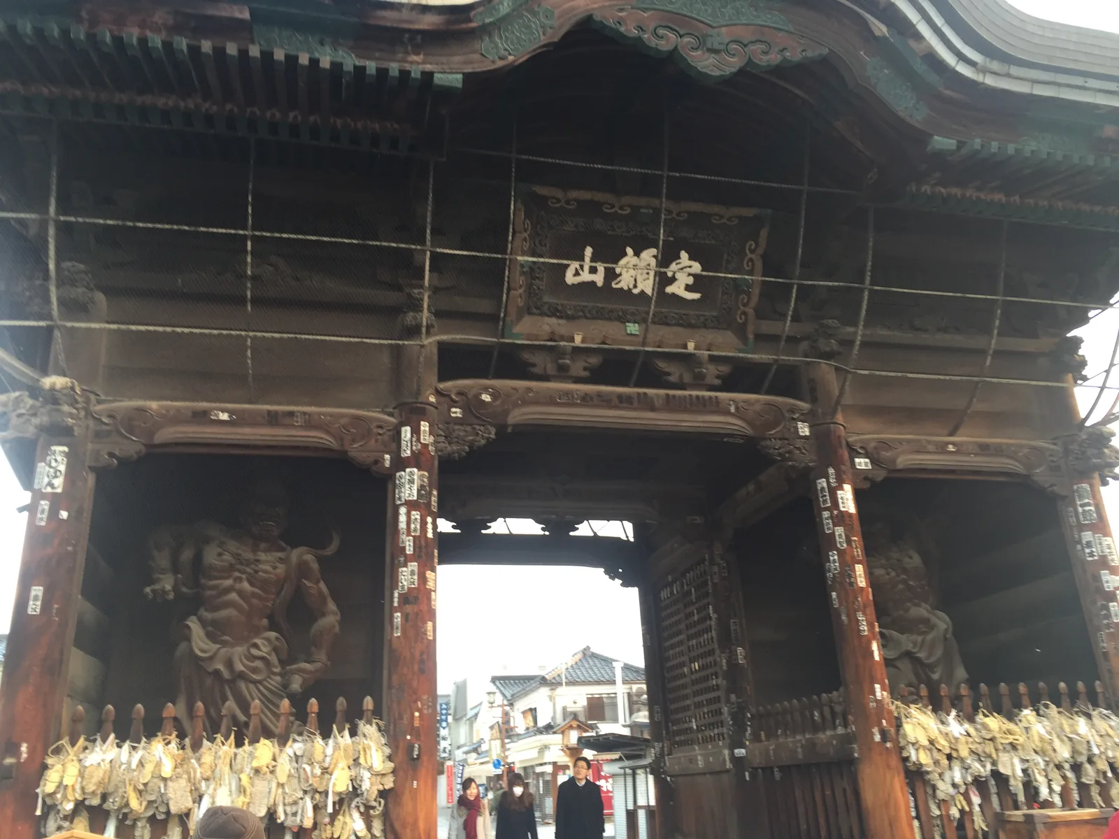 仁王門正面，樓上掛著山號額「定額山」，左右格柵裡是金剛力士像，柵前掛滿了草鞋；門洞另一頭是仲見世的店家