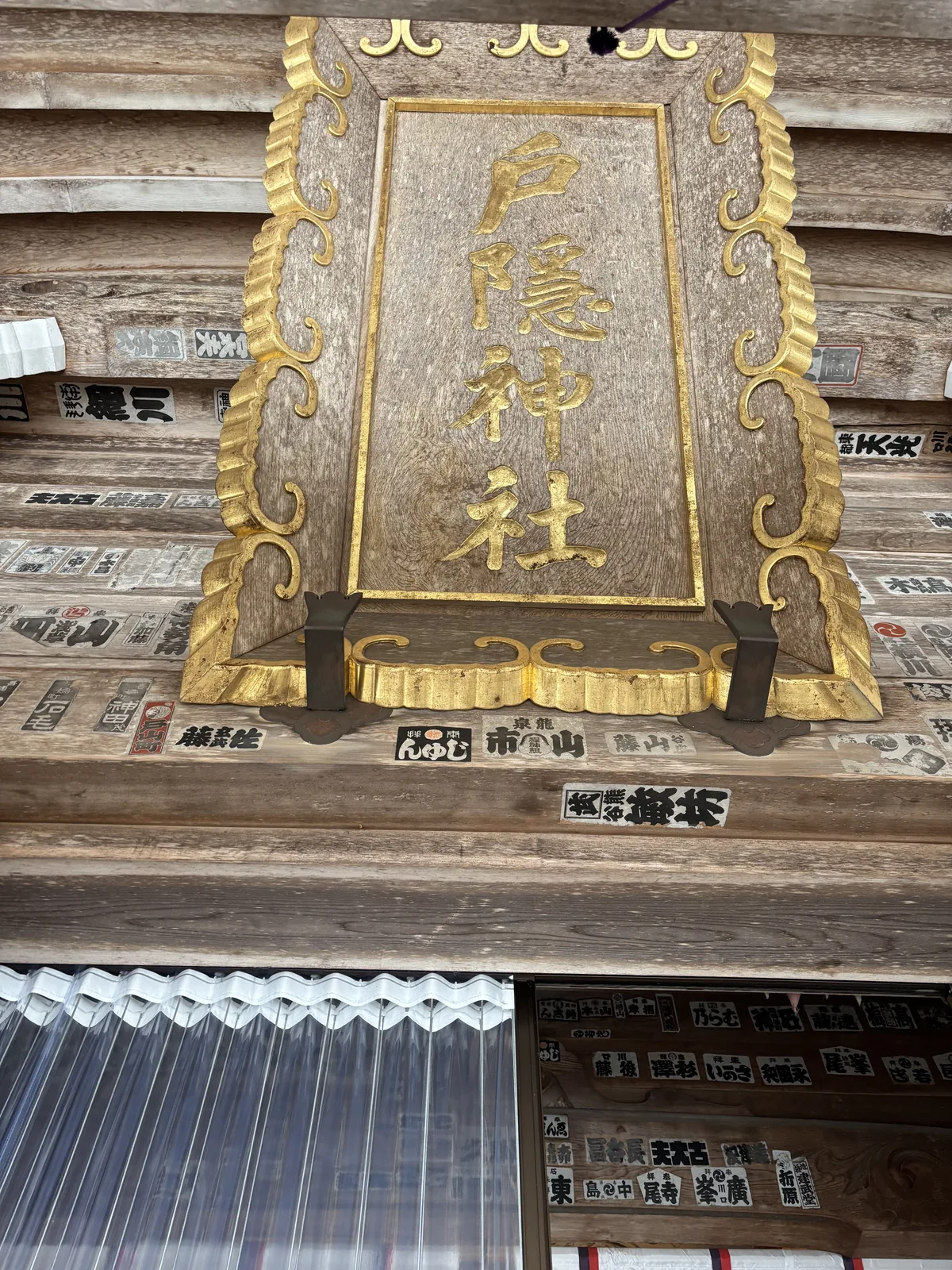 中社拜殿的金色扁額，刻著「戸隱神社」，周圍貼滿千社札