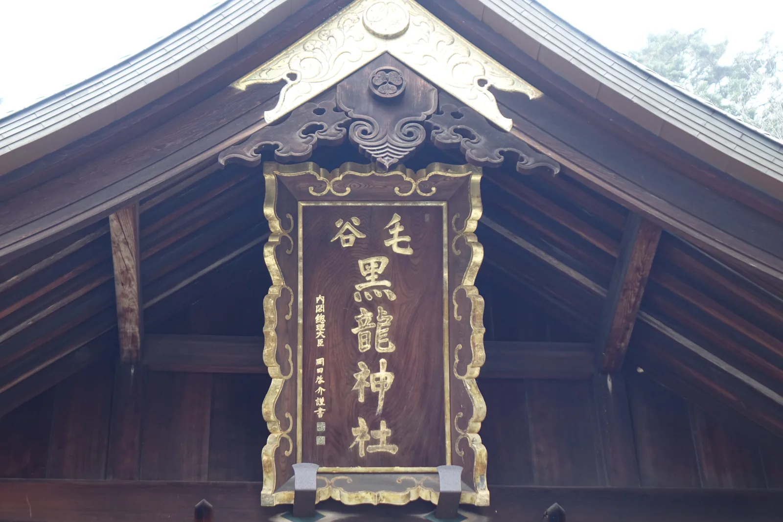 毛谷黑龍神社拜殿破風下的扁額，六個金字嵌在雲龍紋框裡，左側落款「內閣總理大臣 岡田啟介 謹書」