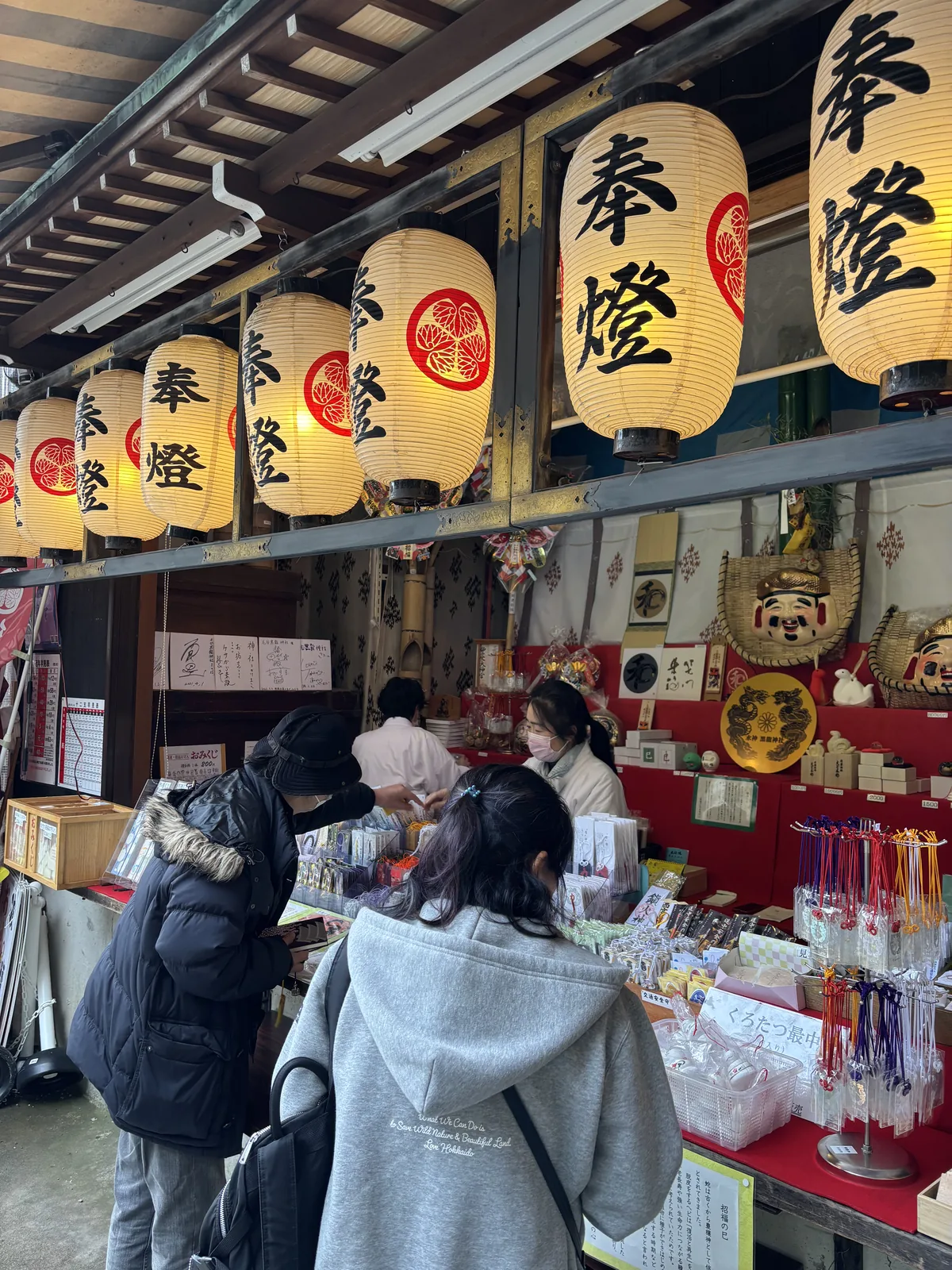 授与所檯面上的御守、破魔矢與緣起物，牆上掛著福面