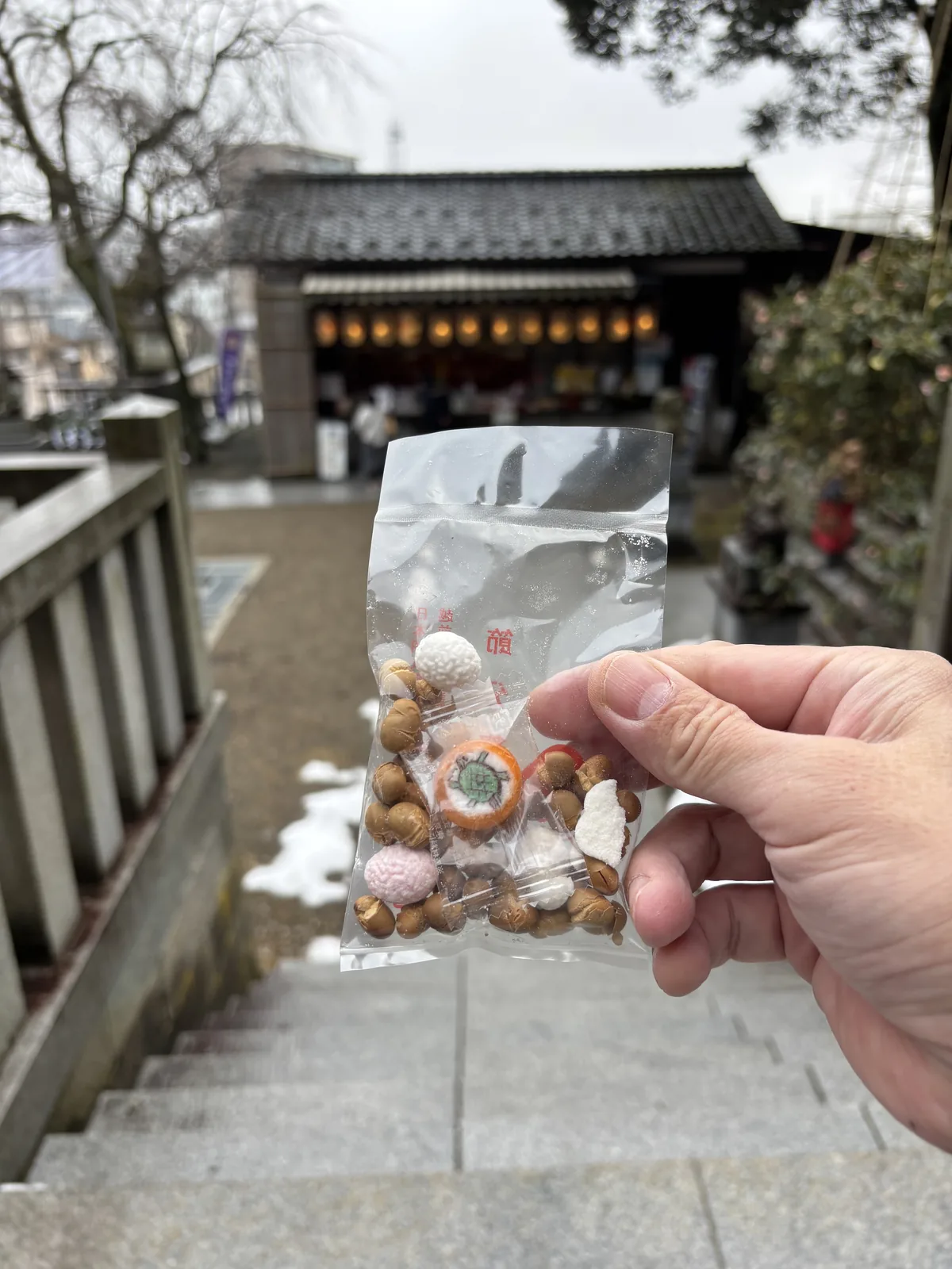 節分祭發的福豆，一小袋豆子與幾個緣起物，背景是往上的石段