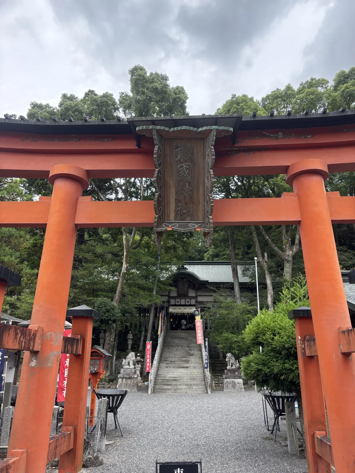 從一之鳥居底下往內看。朱紅的明神鳥居（最常見的鳥居形式），最上面那根笠木之上另加一層瓦頂；正中懸深色的木造扁額，縱書「敢國神社」。碎石參道走到底是石段，石段之上是拜殿。整條軸線短到站在鳥居下就能看完。