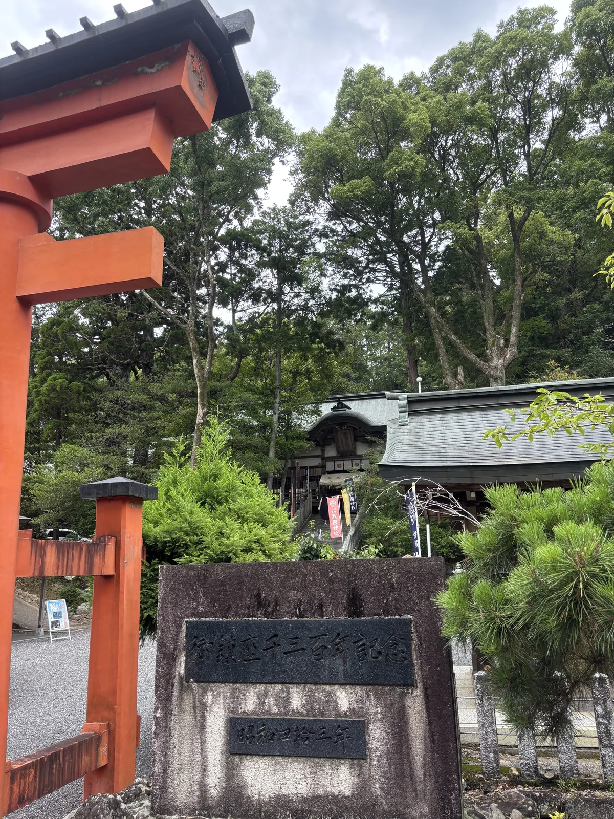 混凝土基座上嵌兩塊黑色石板，上刻「御鎮座千三百年記念」、下刻「昭和四拾三年」——建社一千三百年紀念，一九六八年。左側是朱紅大鳥居的柱腳，右後方是拜殿的簷廊與屋頂。