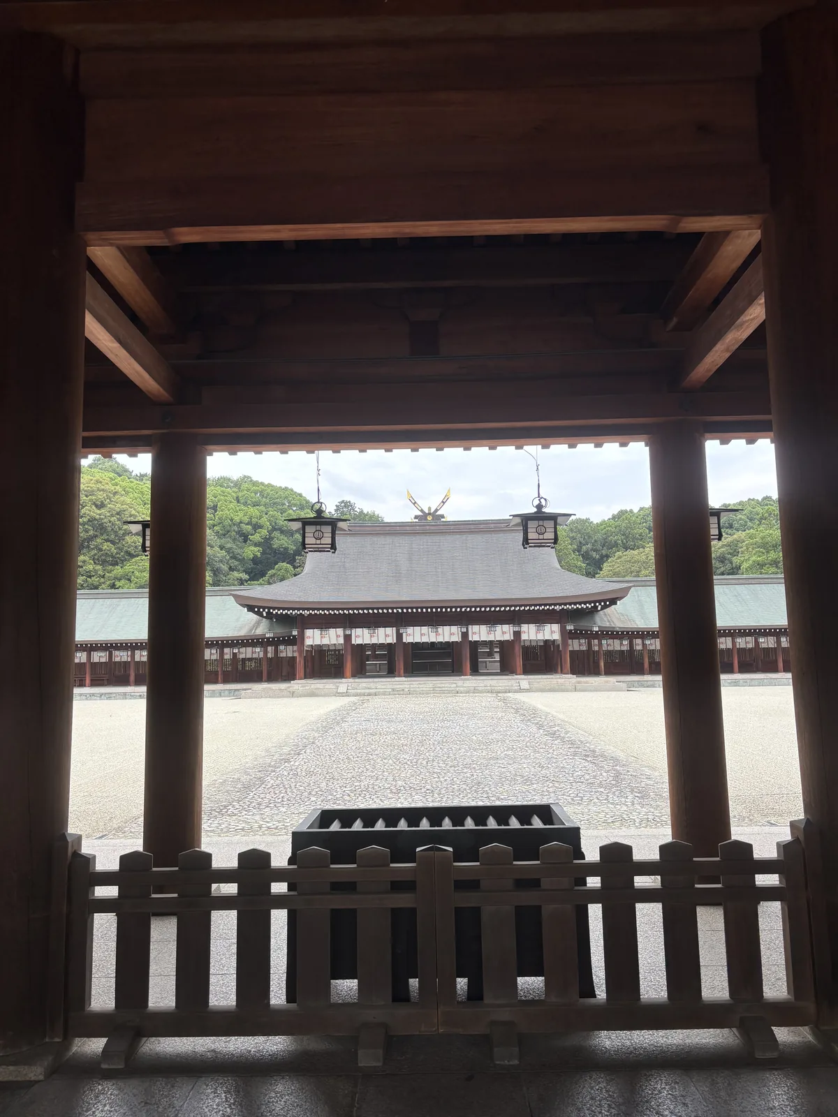 站在南神門之下往外拜殿看。門柱切出一個橫幅，外拜殿的大屋頂剛好落在裡面，門下三盞吊燈籠壓住上緣。中間三千兩百平方公尺的白碎石是外院齋庭——祭典時使用的庭。