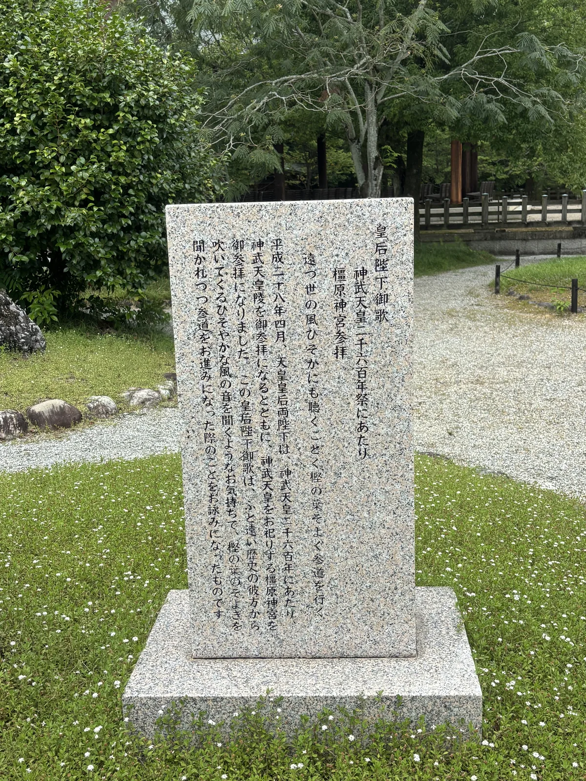 花崗岩碑，刻二〇一六年神武天皇二千六百年祭參拜之後的御歌「遠つ世の風ひそかにも聴くごとく樫の葉そよぐ参道を行く」——彷彿悄悄聽見遠古之世的風，走在樫葉沙沙作響的參道上；並附一段說明。碑立在草地上，後面是碎石小徑。