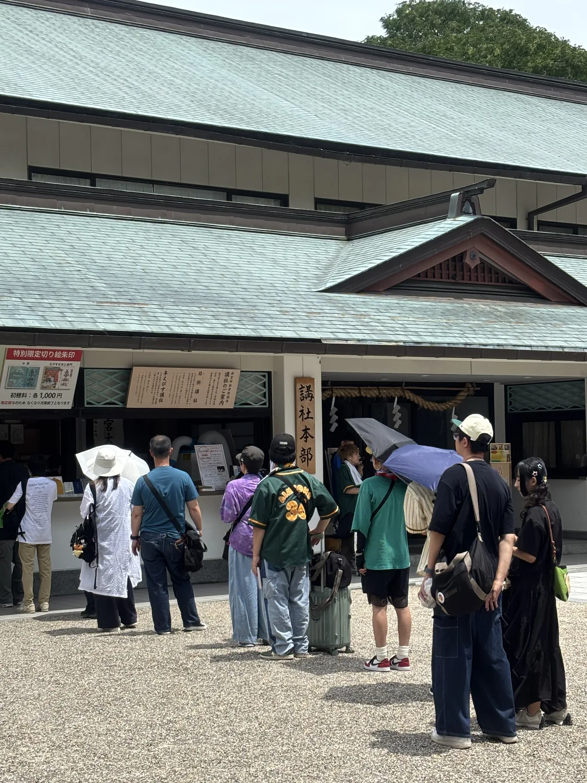 社務所正面，銅板葺的大屋根泛著綠青。門口掛木牌「講社本部」，門楣結注連繩與紙垂。左側掲示〈講社のご案内〉（Kōsha no go-annai，講社導覽）列著崇敬者團體「本えびす講社」「日供講社」；再左一面紅框掲示寫「特別限定切り絵朱印　本殿／えびす宮総本社　初穂料：各1,000円」，並註明限定授與、售完為止。窗口前排著人。