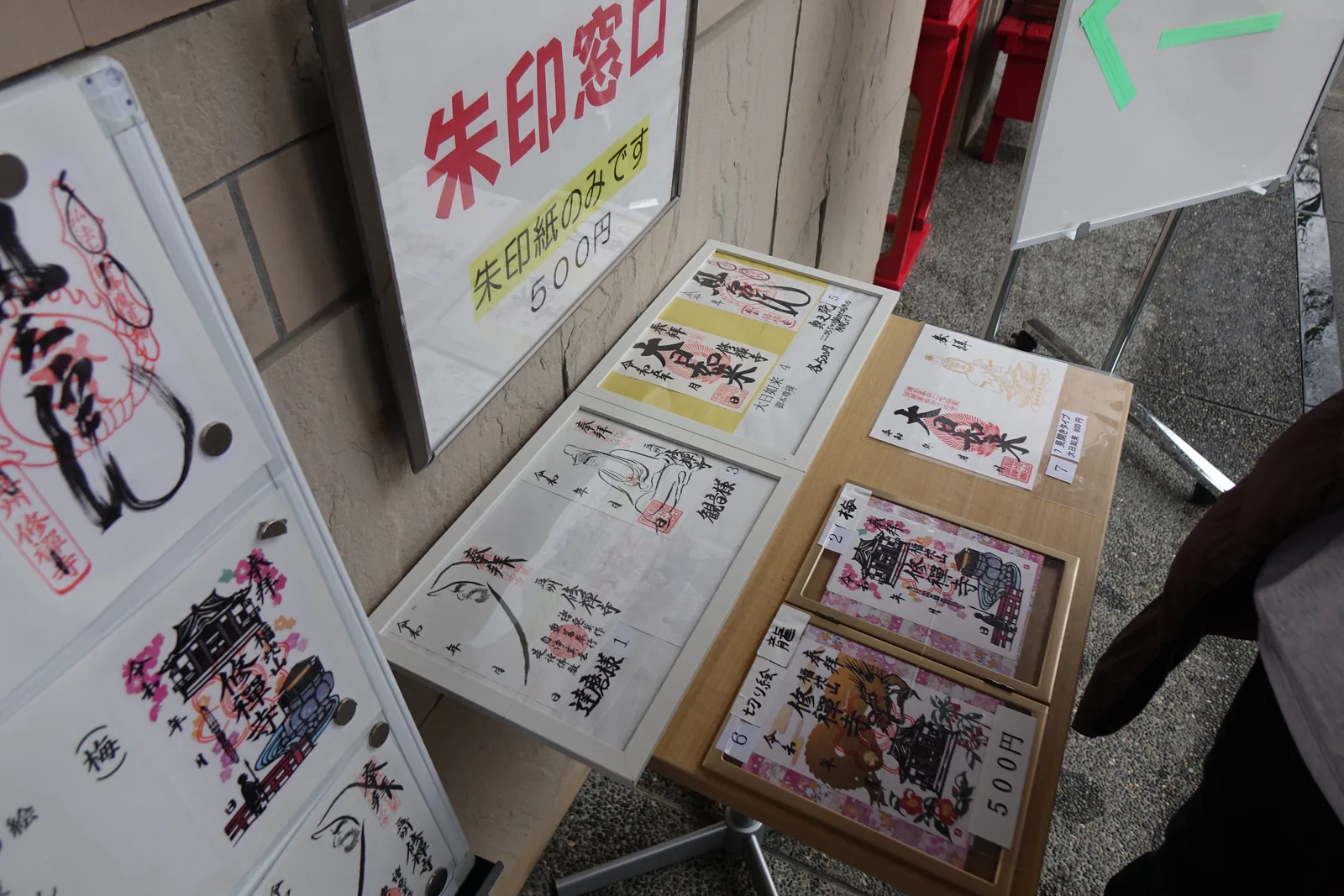 寺務所窗口的朱印樣本，含達磨、觀音與彩色的本堂梅花圖