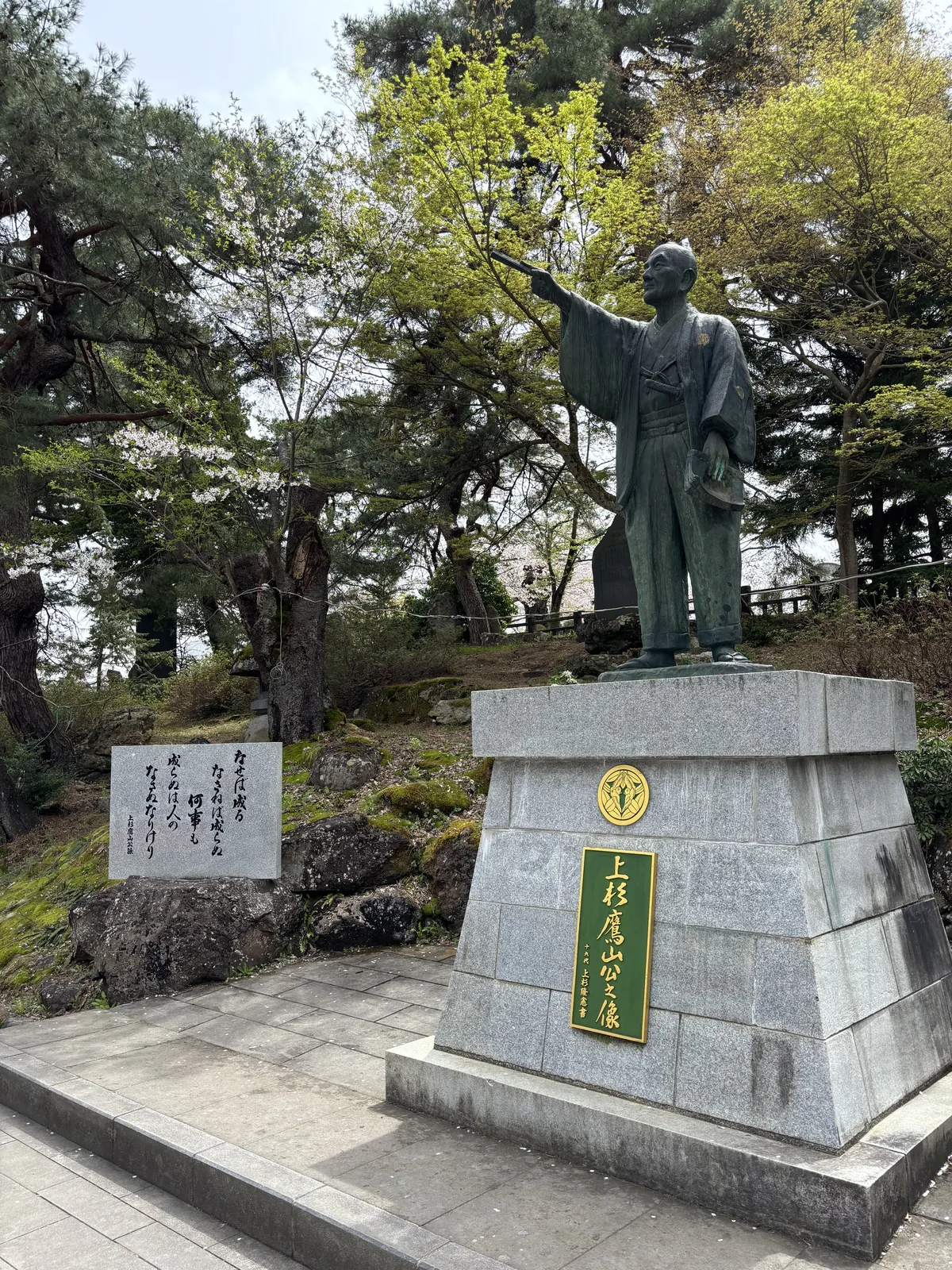 花崗岩台座上一尊立像，和服、右臂高舉指向前方，台座正面嵌「上杉鷹山公像」的金屬字。像後是三株老松與正在開的櫻。這尊是平成四年五月由米澤中央獅子會與上越中央獅子會共同建立的。