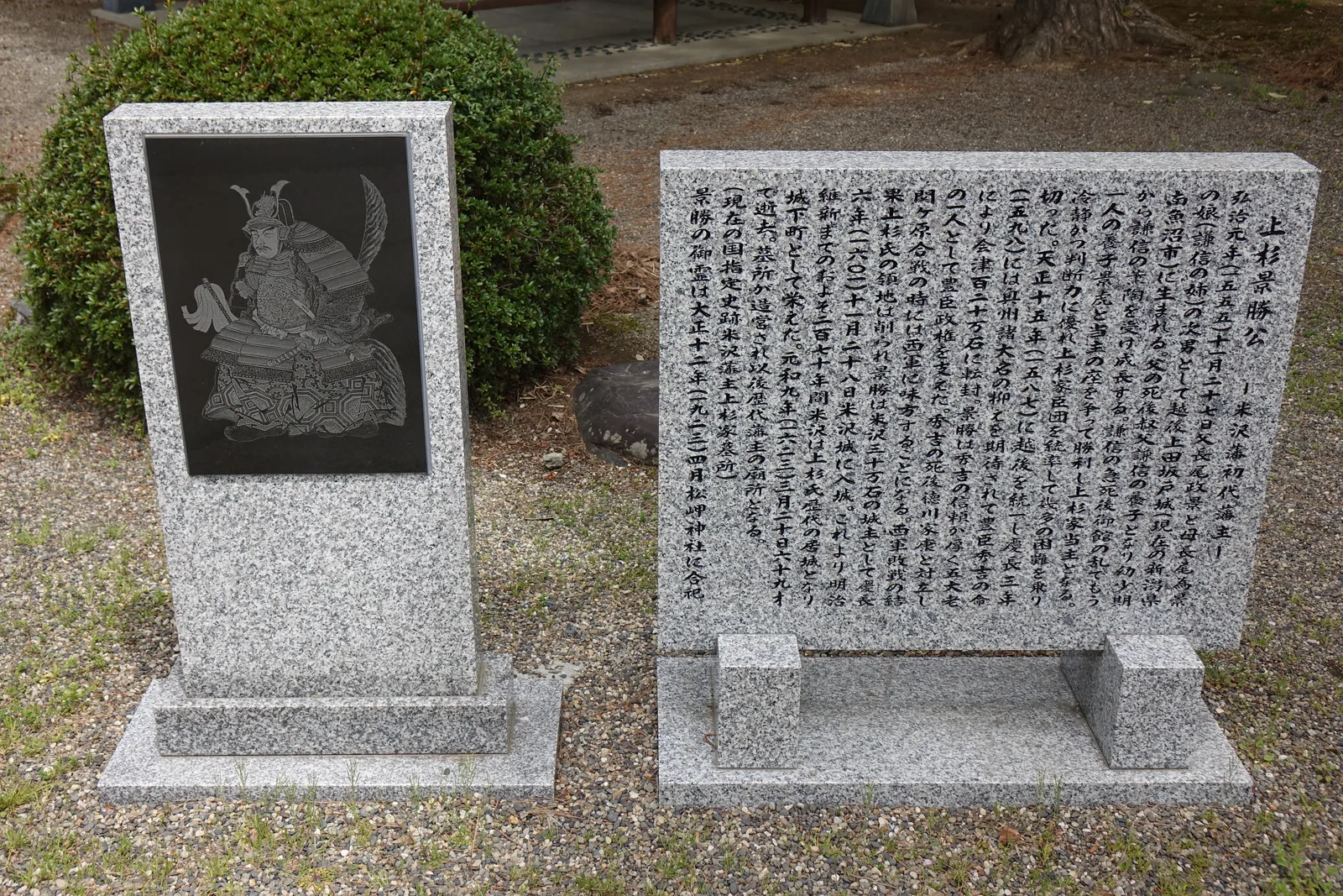 兩座花崗岩碑並列。左碑嵌黑石板，上面線刻著甲冑坐像；右碑整面是碑文，記景勝弘治元年生於越後上田坂戶城、慶長六年十一月二十八日入米澤城、元和九年歿於六十九歲，最後一行寫「景勝の御霊は大正十二年四月松岬神社に合祀」——景勝的神靈在大正十二年四月合祀進了松岬神社。