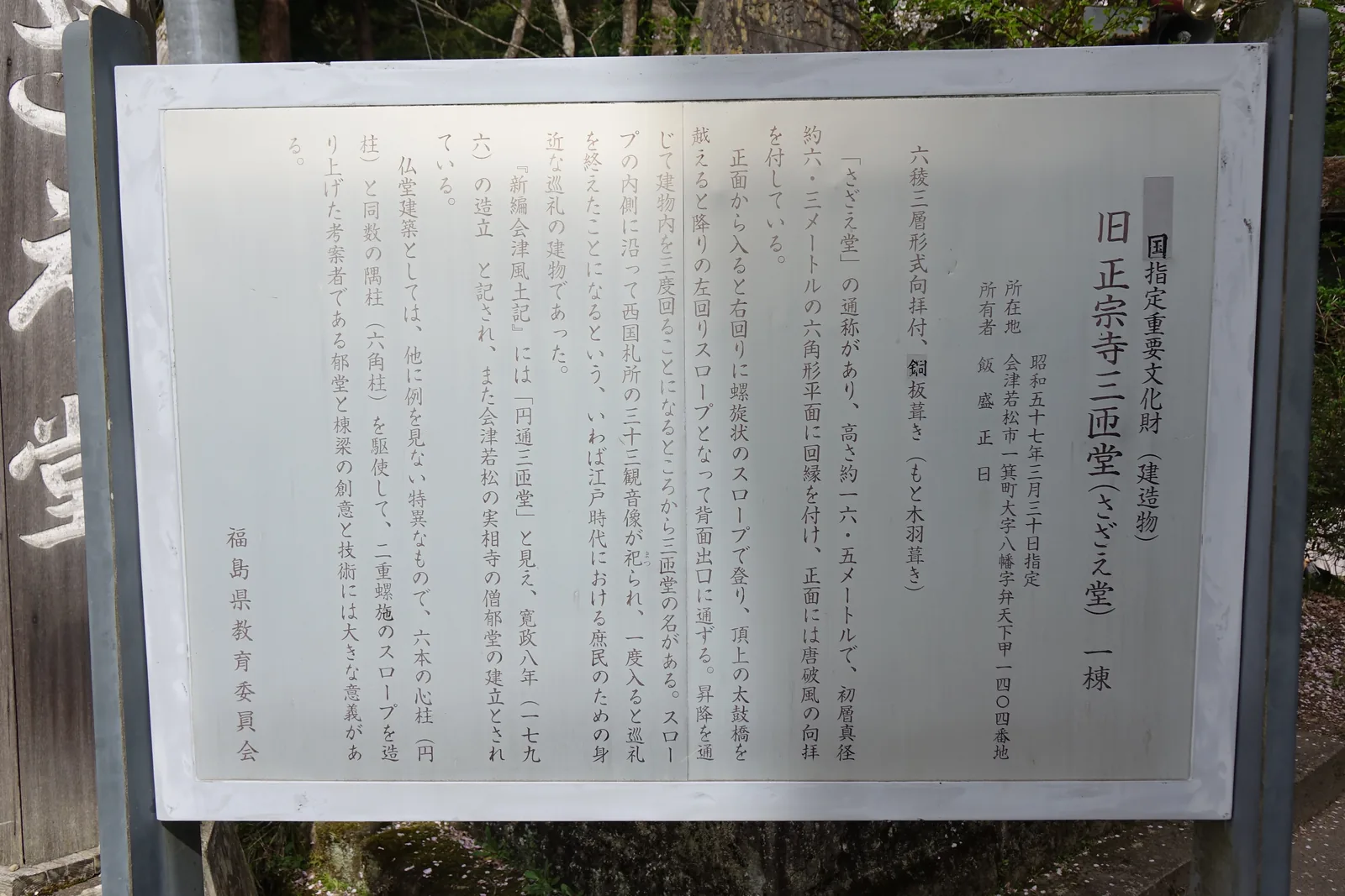 木框裡一面銀色的金屬說明板，直排文字，標題「旧正宗寺三匝堂（さざえ堂）　一棟」，右上小方框寫「国指定重要文化財（建造物）」。文中列出所在地、所有者、形式（六稜三層形式向拝付、銅板葺き），以及六根心柱與六根隅柱的構造說明。落款「福島県教育委員会」。
