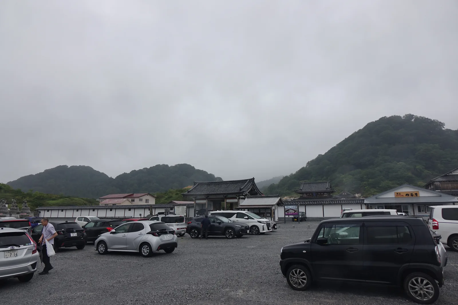 停車場與土塀。白牆黑瓦的一線把境內與外面切開，背後的外輪山整個埋在雲裡。這一天下著雨。