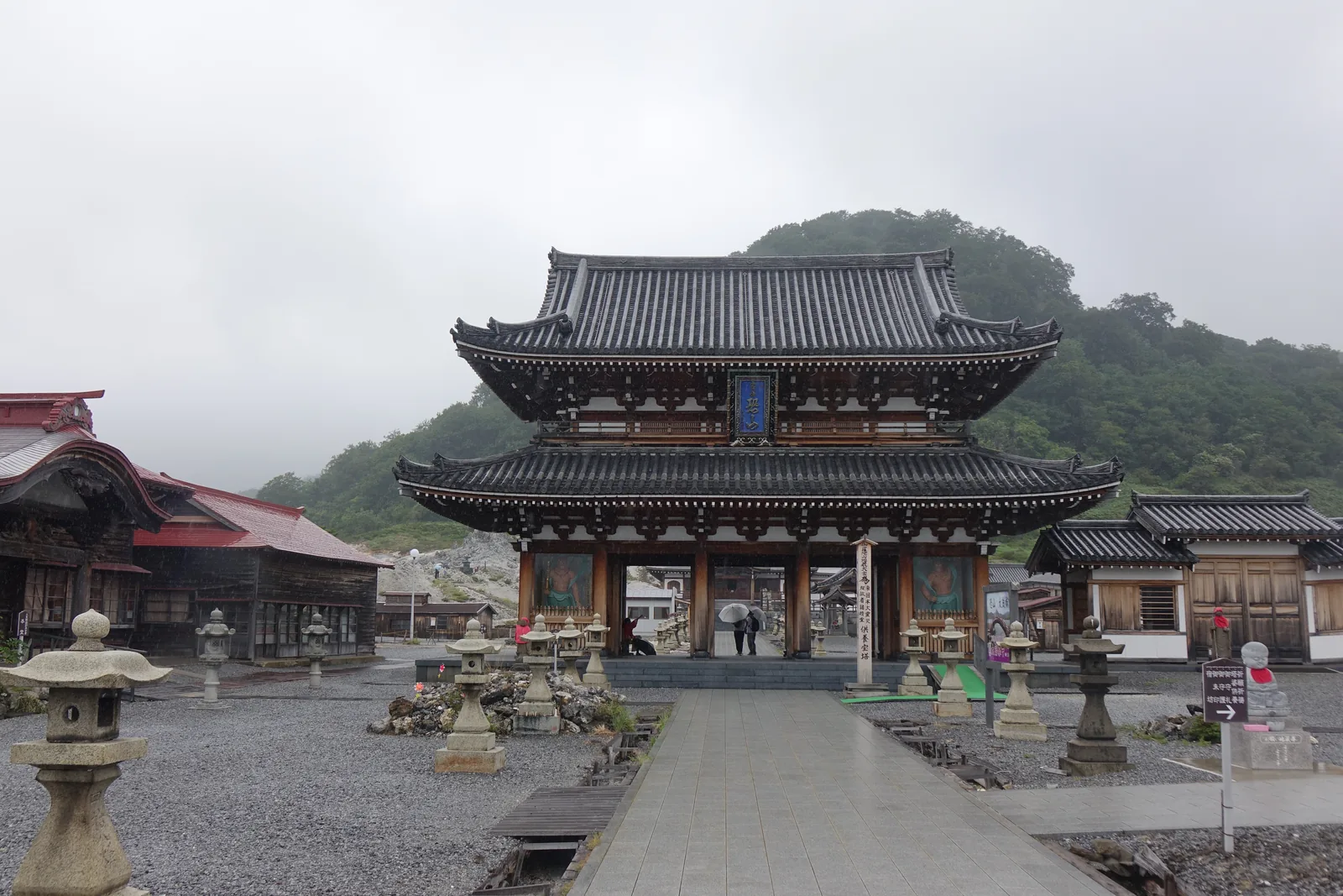 兩層的樓門正面，下層左右是仁王像，樓上掛著直式的藍底匾，題「恐山」——曹洞宗大本山第七十八世貫首宮崎奕保禪師的親筆。前方地面散立著石燈籠與小塔。