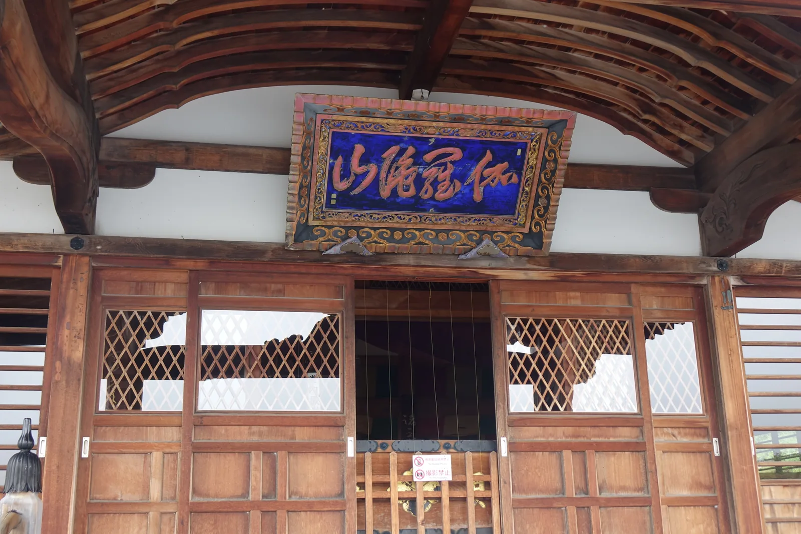 地藏殿正面的橫匾，藍底朱字題「伽羅陀山」——佛典裡地藏菩薩所居之山，也是正式名「恐山伽羅陀山菩提寺」的中段。匾下是格子戶，貼著禁止攝影的告示。