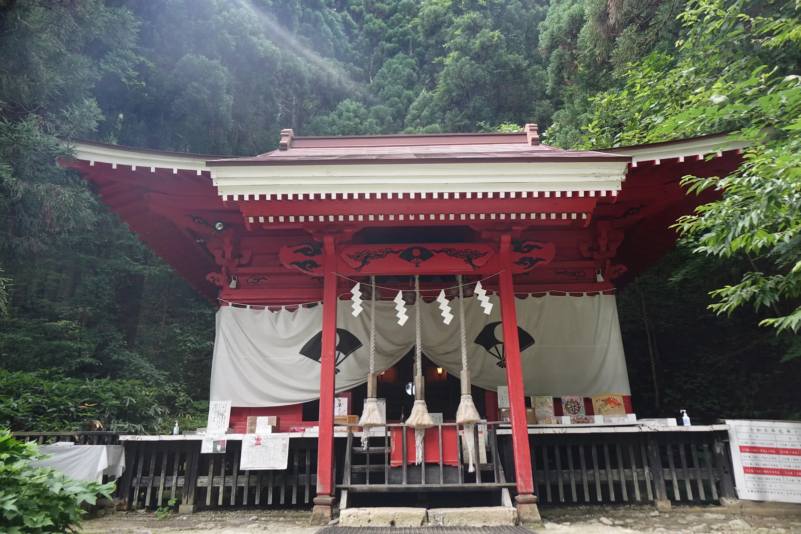 拜殿正面。整體朱塗，銅板葺的屋頂配白色的破風（hafu，屋頂山牆）飾帶，簷下一道白色鋸齒狀飾列；蟇股與木鼻上全是黑色雲紋雕刻。正面垂白幕、染成對的黑色紋樣，三束鈴緒垂在中央，前緣是塗黑的玉垣。