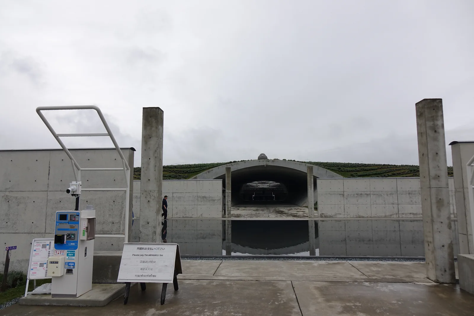 頭大佛殿入口的自動精算機、對講機與監視器立在清水混凝土牆前，機身印著「墓園利用者は拝観料無料」