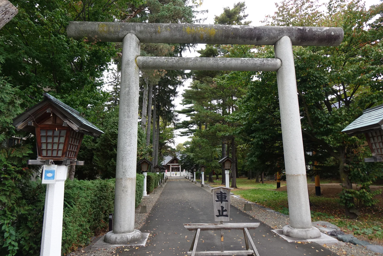 富良野神社參道入口，兩座石造明神鳥居前後疊在一起，左側是木造覆屋式燈籠，地上橫著寫「車止」的木牌