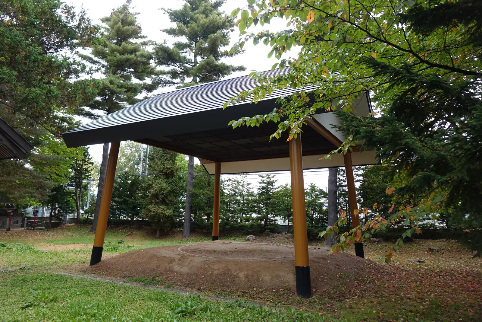 富良野神社境內的土俵，四根黃柱撐起黑色方形屋頂，下面是一圈新培的土