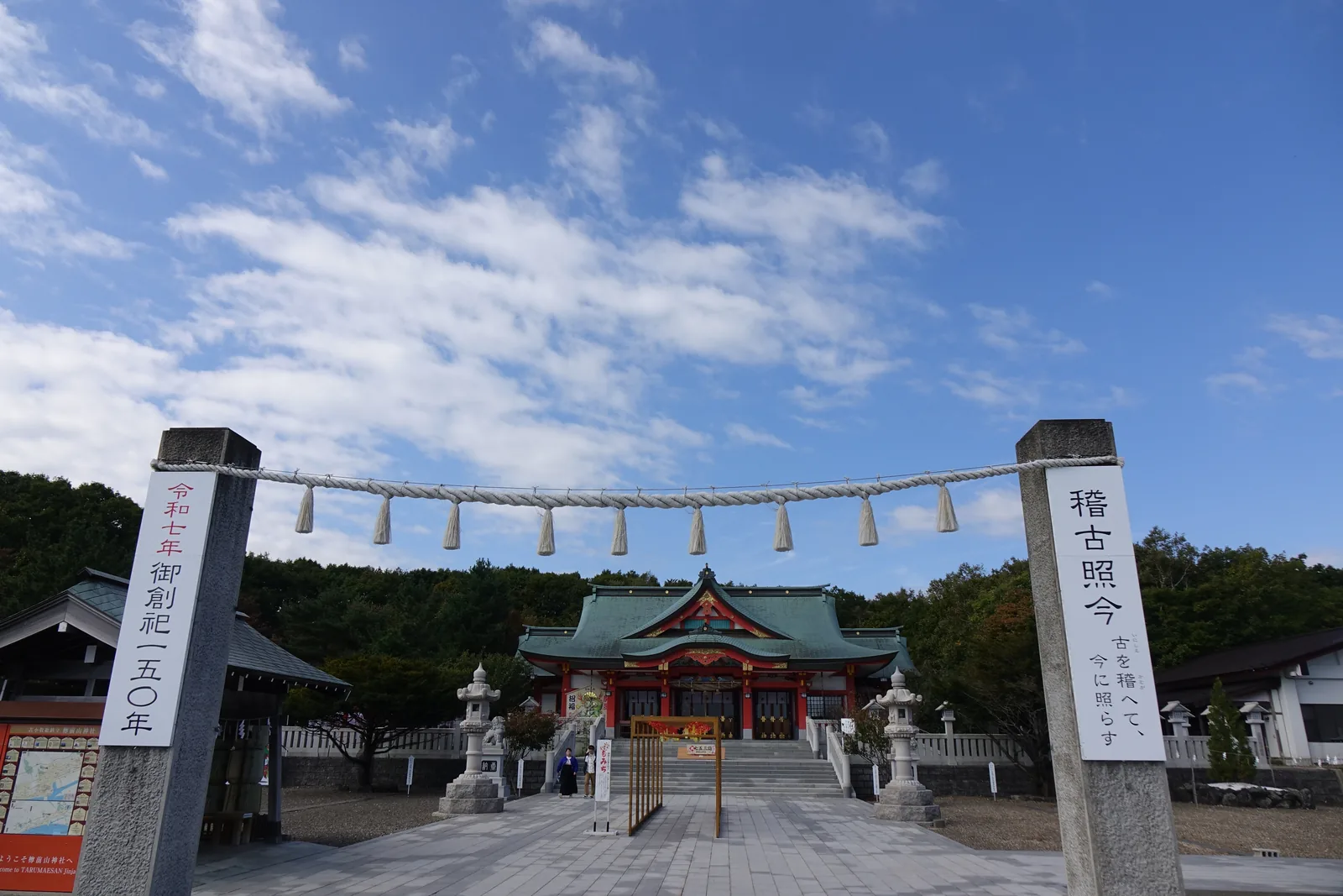 樽前山神社入口的兩根石造注連柱，中間橫著注連繩，右柱掛板寫「稽古照今」，左柱掛板寫「令和七年 御創祀一五〇年」