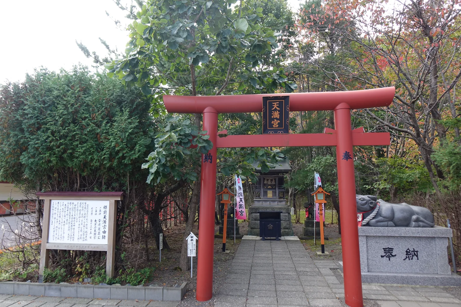 樽前山神社境內社樽前天滿宮的朱鳥居，扁額寫「天満宮」，右前方是石造的臥牛與奉納台座，左側立著木造由緒板