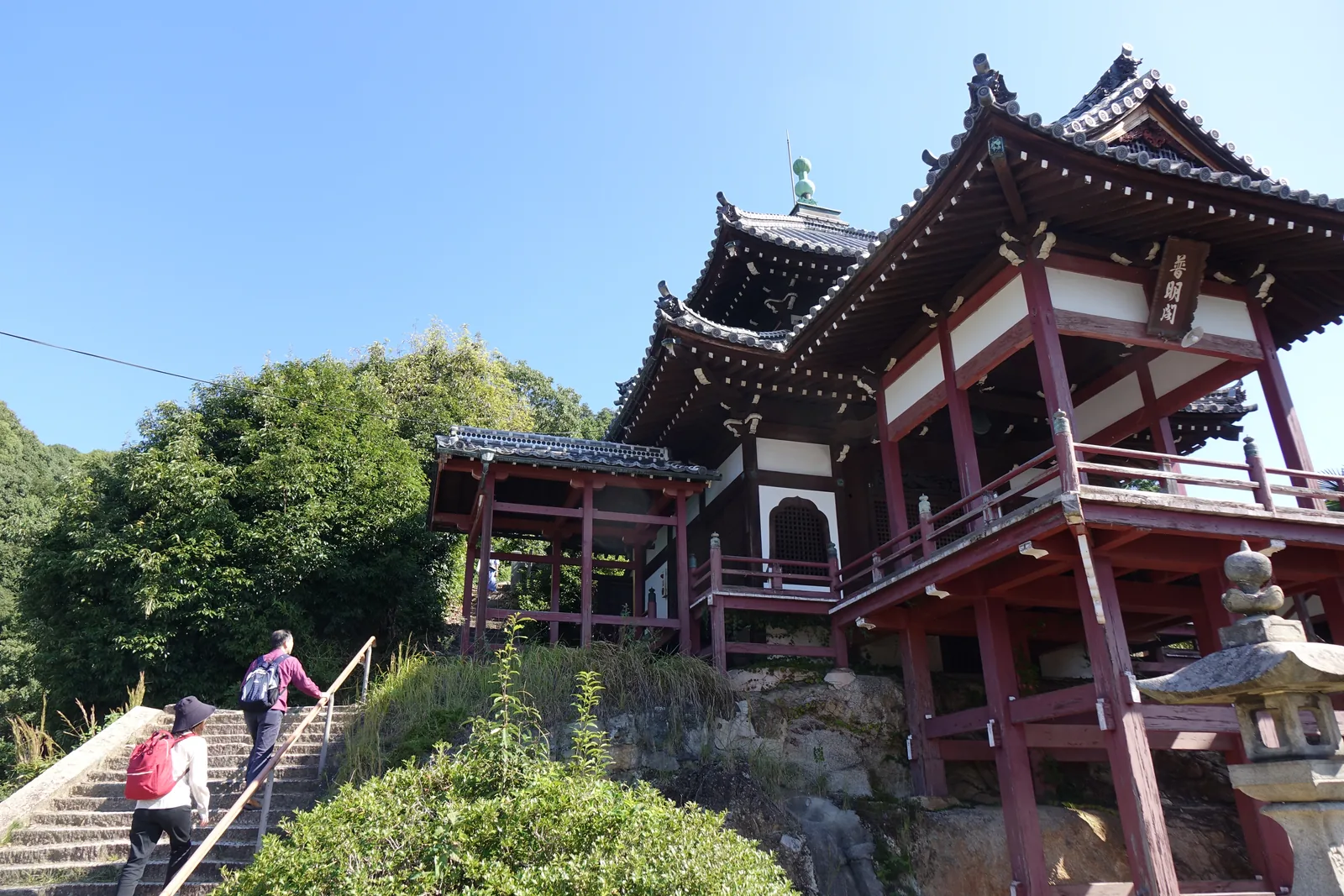 西方寺境內的普明閣，朱色的柱與貫架在岩盤上，方三間的堂體整個推出台地邊緣，二重屋根是本瓦葺