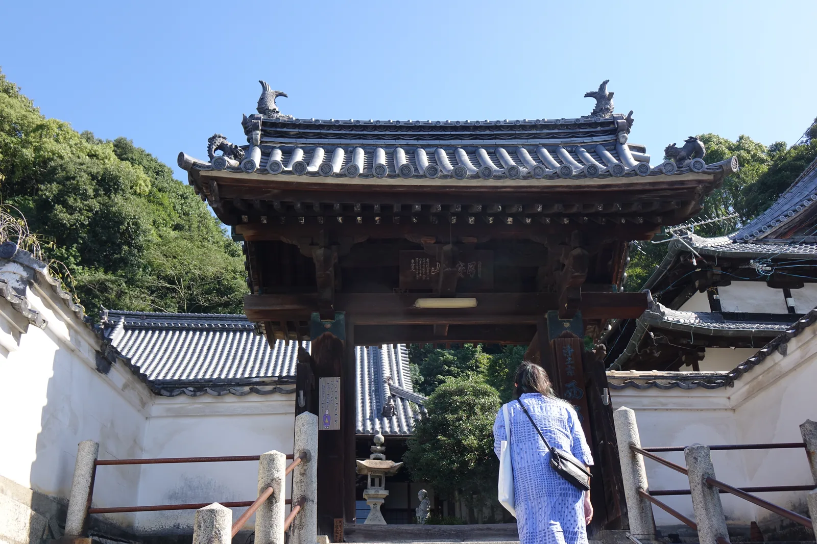 西方寺山門，本瓦葺，屋脊兩端立著獸形棟飾，四角是龍形鬼瓦，兩側接上白色築地塀