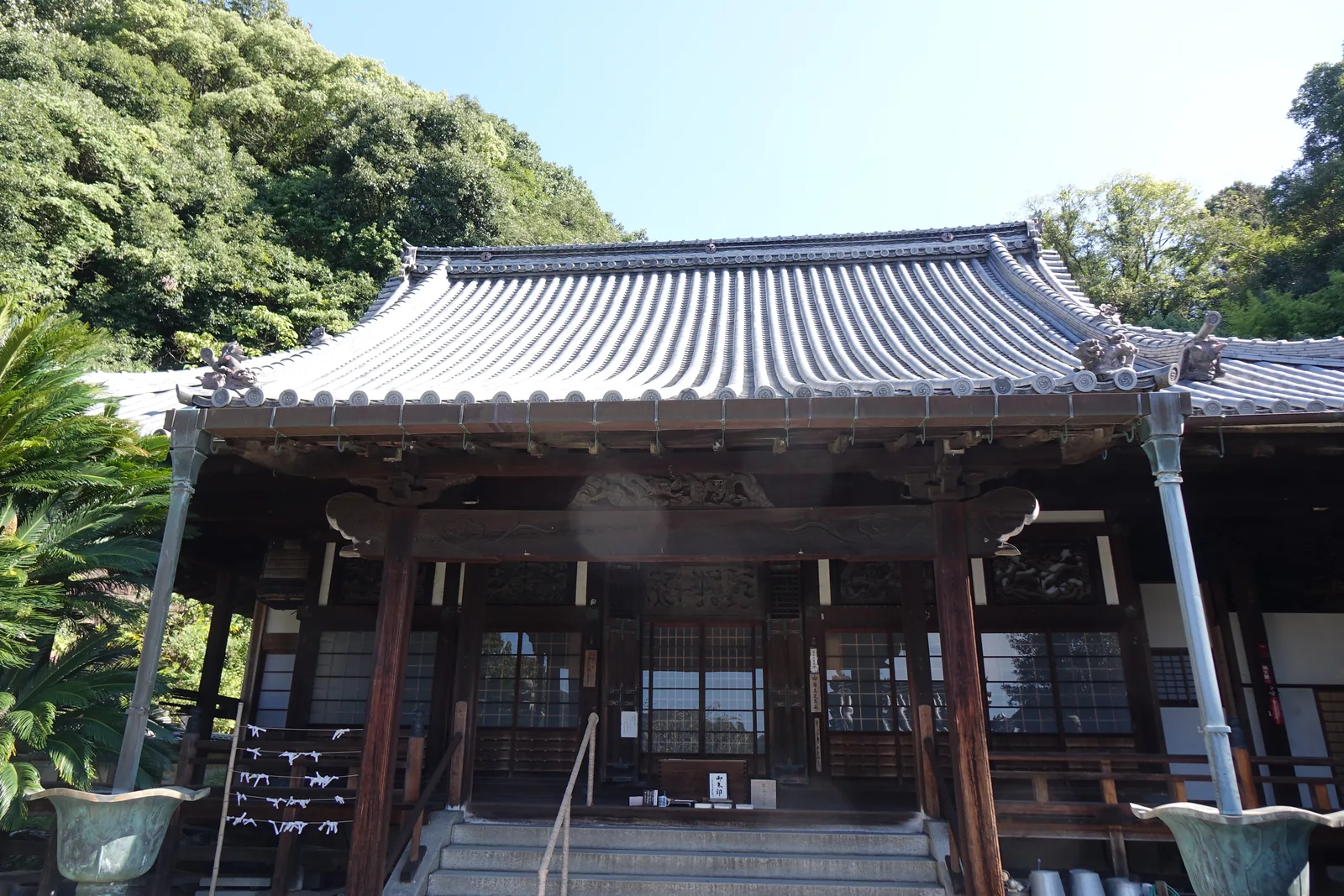 西方寺本堂正面，入母屋造本瓦葺，前面與側面前方做成吹拔不設牆、只有一整排柱子，階的左側長著一株蘇鐵