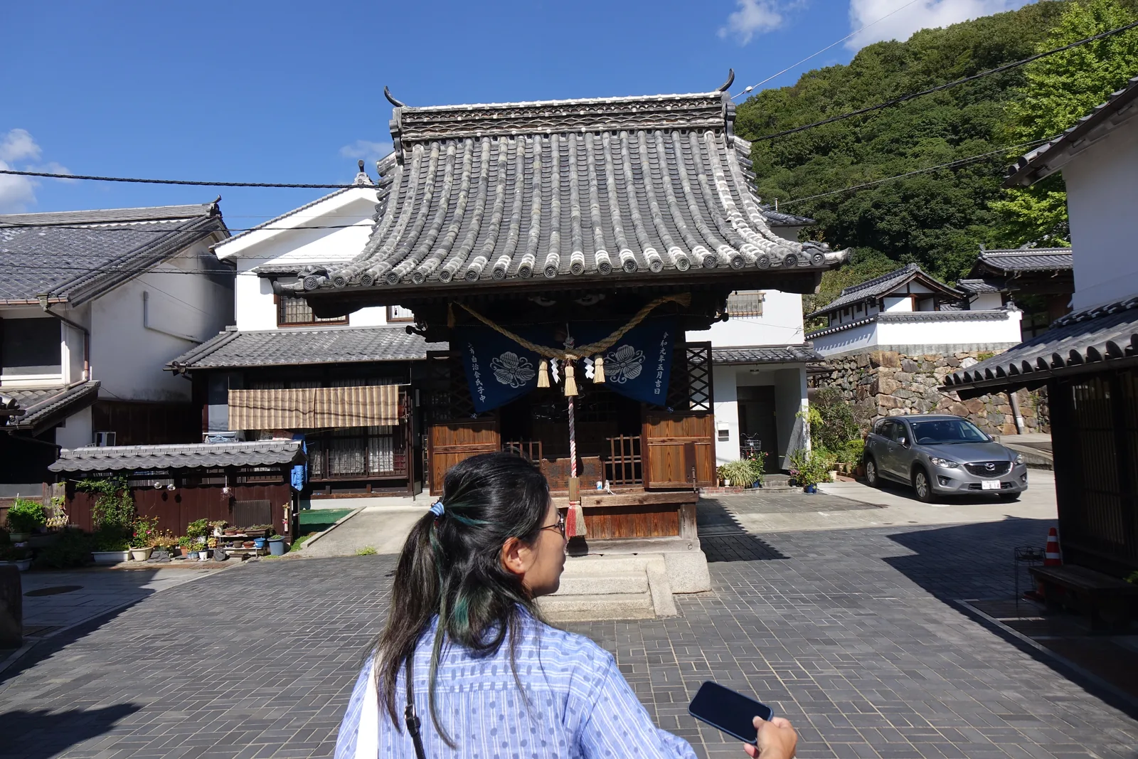 町並み北段小路上的一間小堂，入母屋造本瓦葺，注連繩下垂著紙垂，紺色的幕上白染家紋