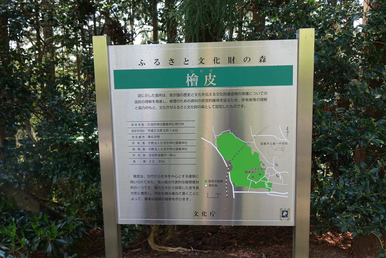 一塊不鏽鋼的解說牌立在常綠樹叢前，標題「ふるさと文化財の森」，綠色橫幅上是「檜皮」二字。左欄記設定名稱「志波彦神社鹽竈神社境内林」、平成二十九年三月十四日、第六十九號、面積二十二點三公頃；右邊是一張綠色標出設定範圍的地圖。發行單位是文化廳。