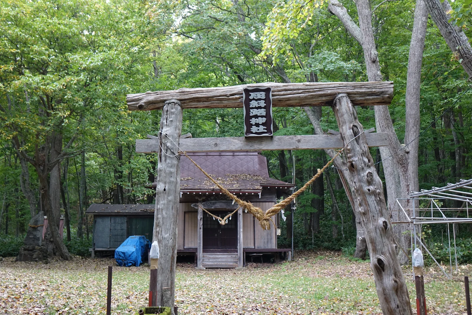 屈斜路神社的鳥居與社殿，鳥居的三根木材都保留著樹皮與節疤，注連繩從兩根立柱之間拉過去，笠木正中的扁額刻「屈斜路神社」