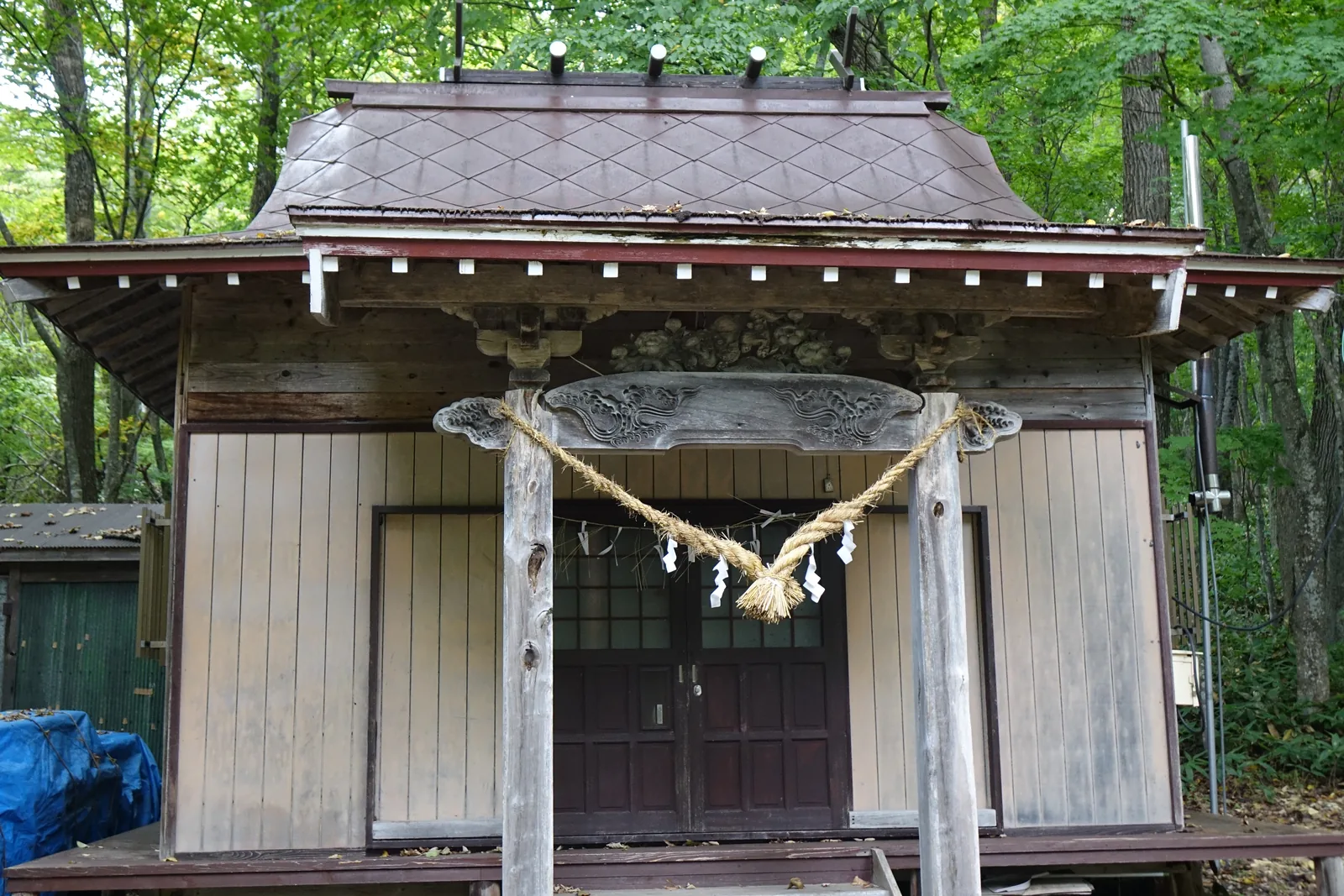 屈斜路神社的社殿正面，銅板葺的屋頂氧化成暗紅褐色、鋪面壓出菱形接縫，向拜底下的欄間雕著波浪，牆是縱向板張