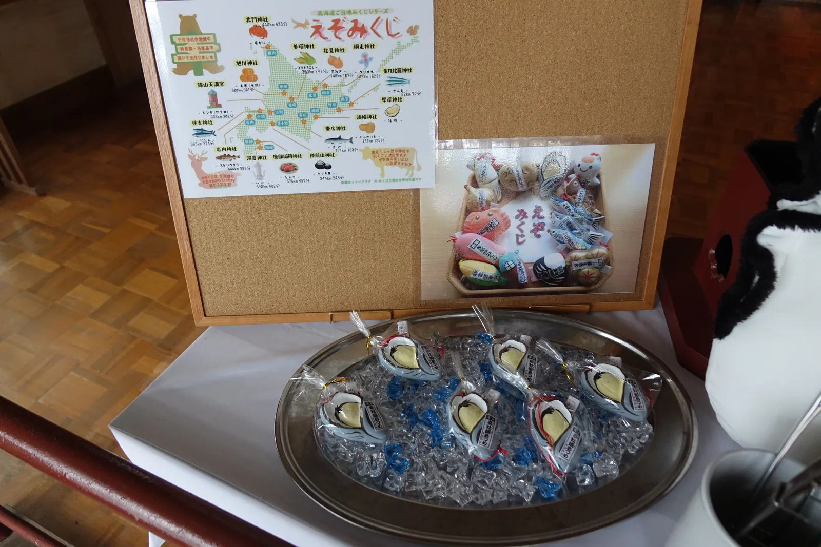 厚岸神社的幸牡蠣あつめみくじ（sachi-kaki atsume mikuji，招福牡蠣御神籤）：銀盤上鋪著透明碎冰，包裝好的牡蠣形御神籤像生蠔一樣攤在上面，後面貼著「北海道ご当地みくじシリーズ えぞみくじ」的道內分布圖