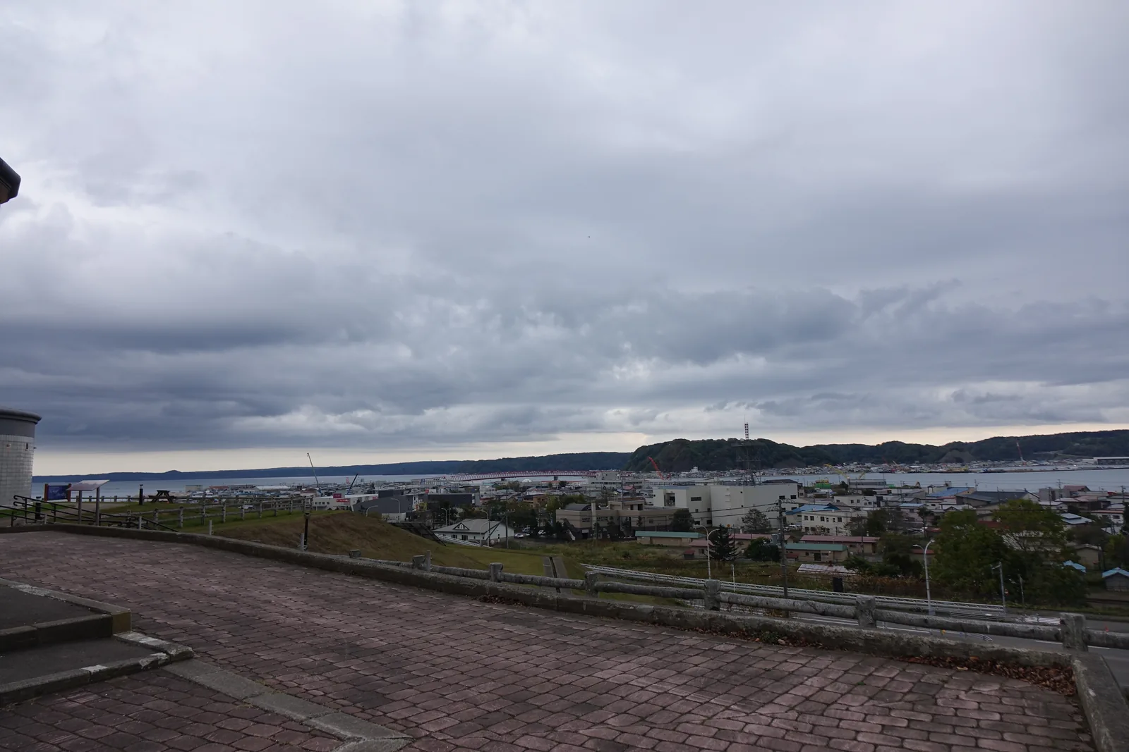 從道の駅厚岸グルメパーク的磚鋪露臺望出去，欄杆外是整片厚岸市街的屋頂，再過去是一道低矮的岬與開闊的水面