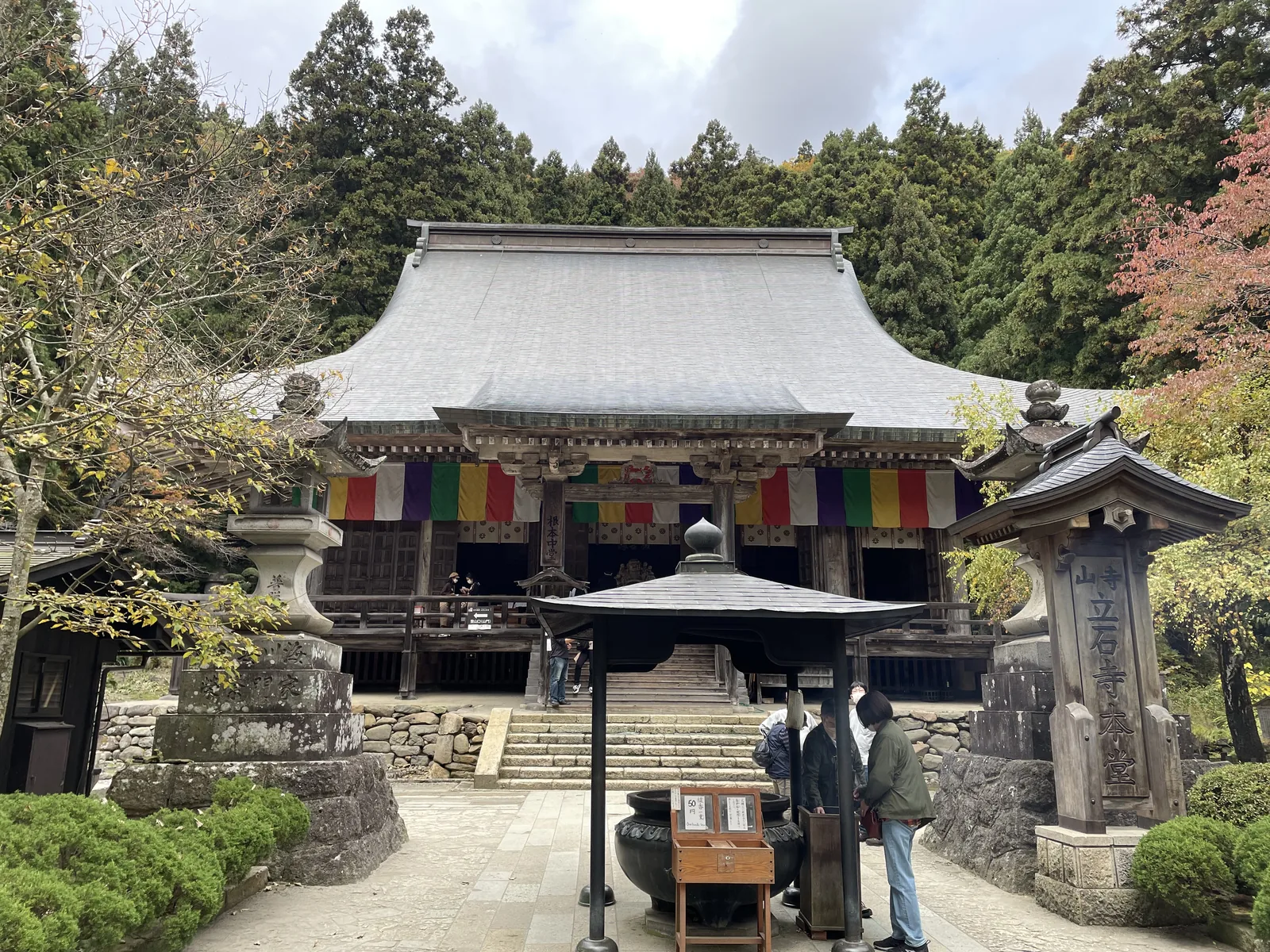 延文元年（一三五六）山形城主斯波兼賴再建，入母屋造、五間四面，據說是日本現存最古的山毛櫸木建築。簷下掛著五色幕，堂前立石標刻「山寺　立石寺本堂」，右側石燈籠與香爐之間就是參拜的軸線。這一棟在收費的山門之外，任何人都能走到它前面。
