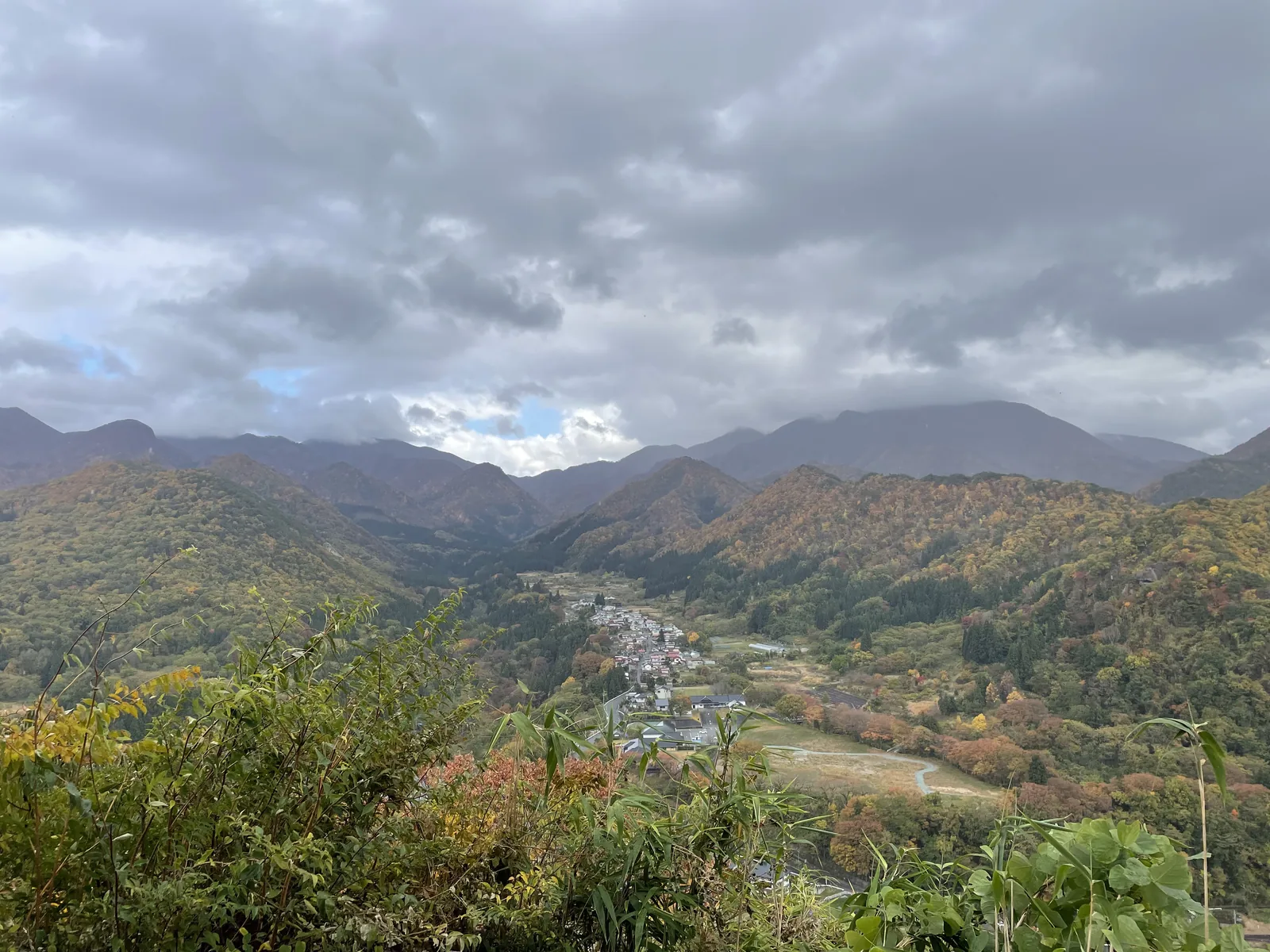 山寺盆地與對面的山稜，樹色從橘到褐，雲層壓得很低。五大堂是舞台造，整座挑出崖外——全山唯一一棟往外看的建築，也是最高、最晚走到的一棟。