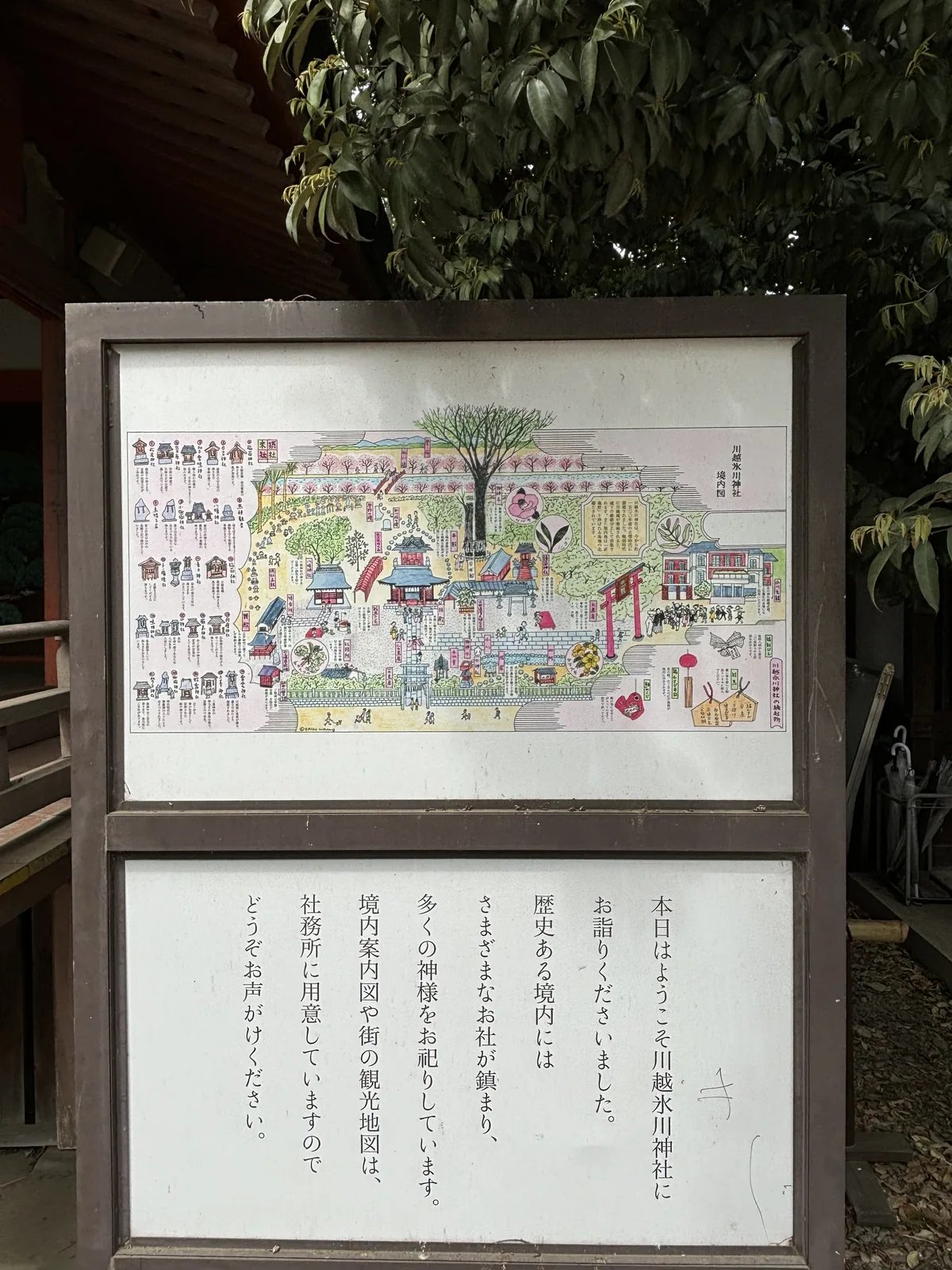 木框裡上下兩面板。上面是手繪的彩色境內圖，右上角直書社名與「境內圖」三字，畫著社殿、鳥居、末社群與參拜的人，左側一欄逐一標出末社的名字。下面那塊直書「本日はようこそ川越氷川神社にお詣りくださいました」，意思是歡迎今日前來參拜，並說境內鎮座著許多神明、社務所備有境內案內圖與市街觀光地圖。
