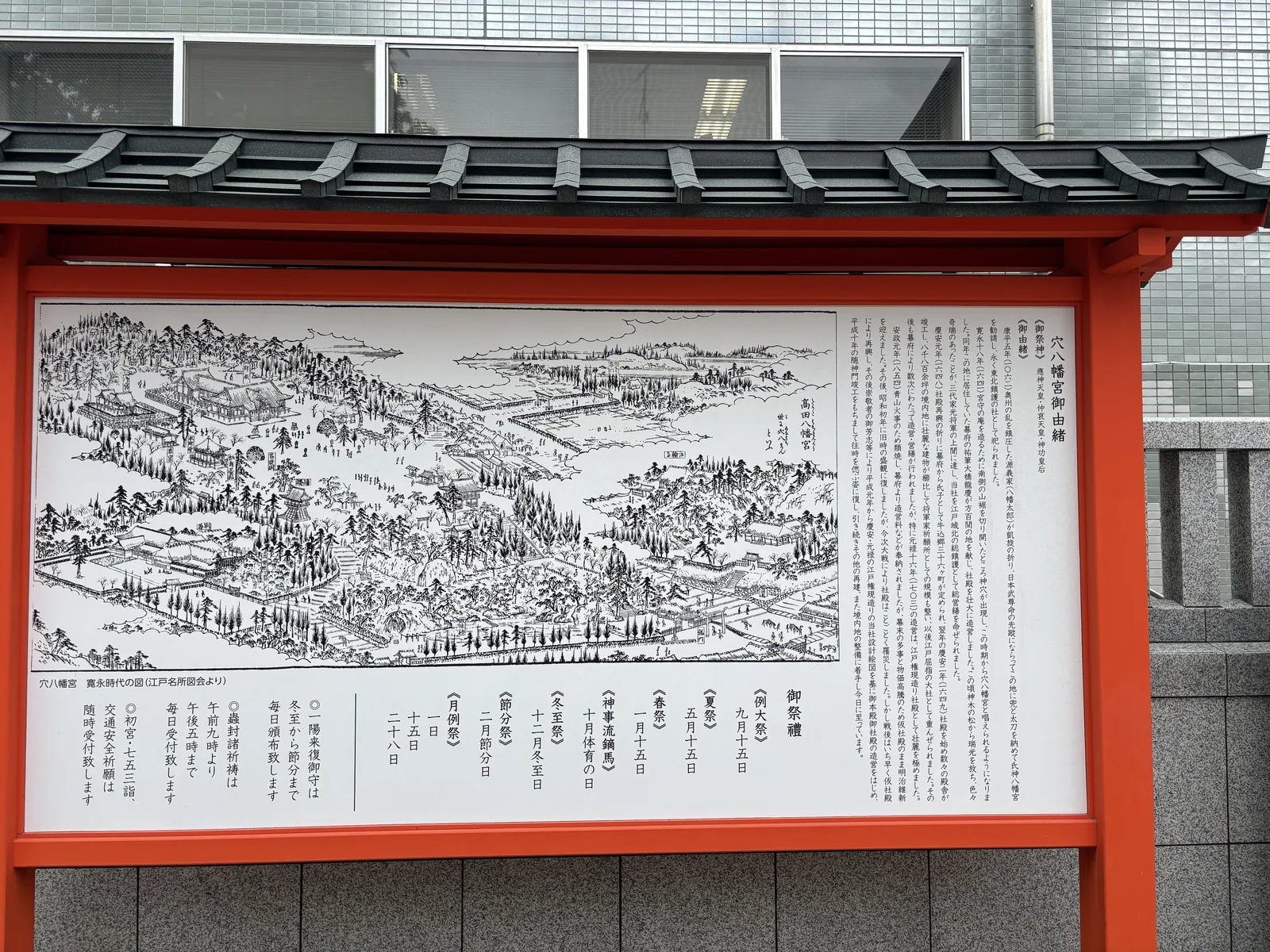 從稍遠處看那面朱漆框的掲示板。黑瓦的小屋頂下是一整面白板，左半的鳥瞰圖與右半的直書文字各佔一半。板下是灰色的石砌基座，背景是現代大樓的磁磚牆、窗與空調管線。