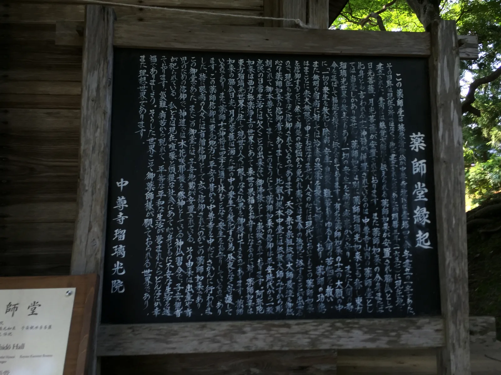 「藥師堂緣起」的黑色說明板，立在木框裡，白字密密寫滿整面，左下另立一塊小牌