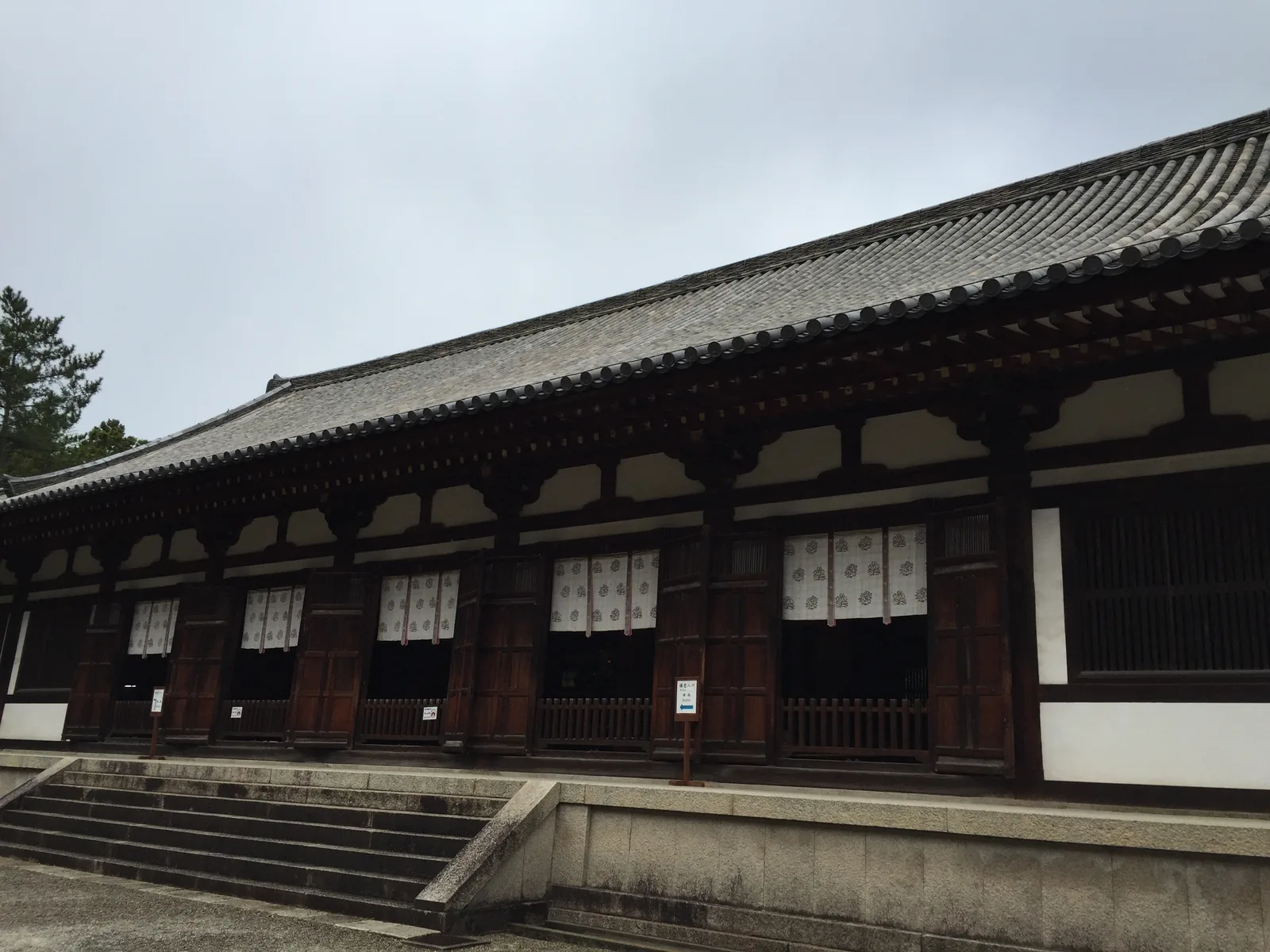 唐招提寺禮堂與東室的長側面：南北向十九間的細長建築，一整排柱間垂著白色的幕，白壁與深色木構交替，底下是低矮的石造基壇
