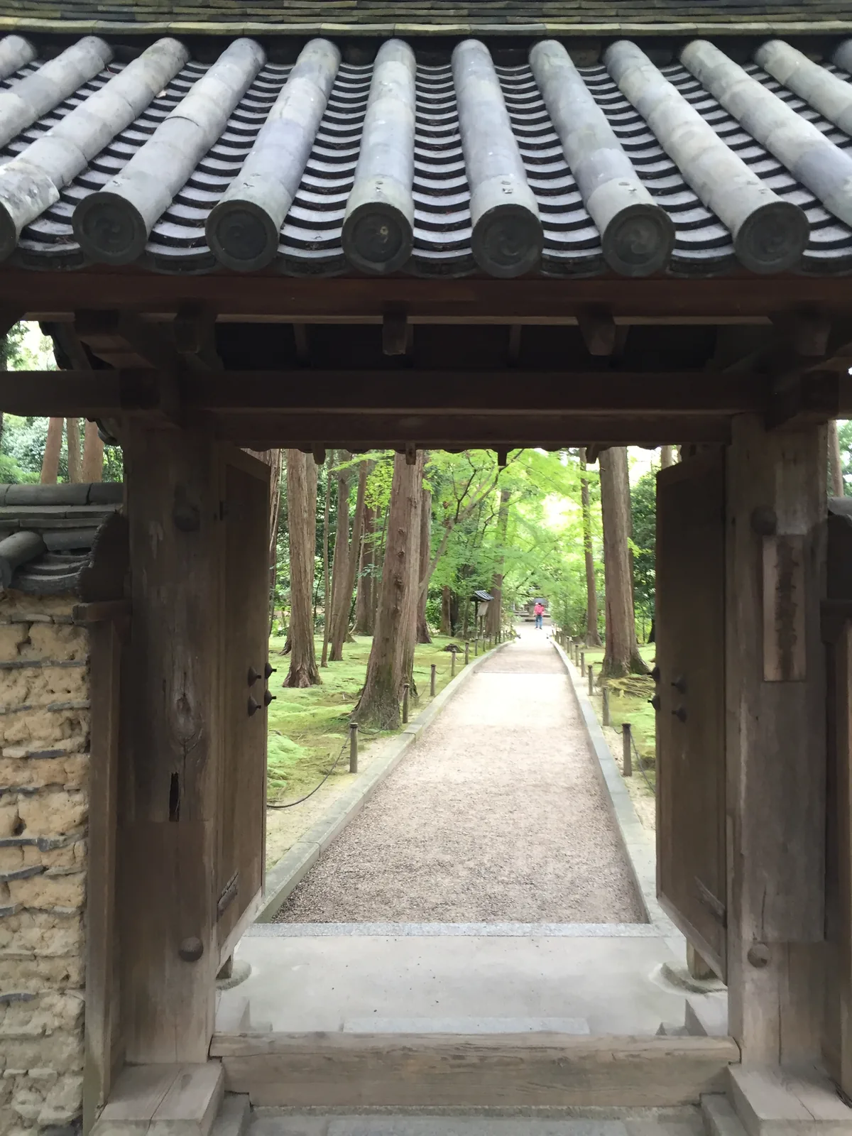 從唐招提寺御廟的門下望出去：門框把一條砂路裁成長方形，兩側是修剪過的苔地與樹，路一直延伸到很遠的盡頭