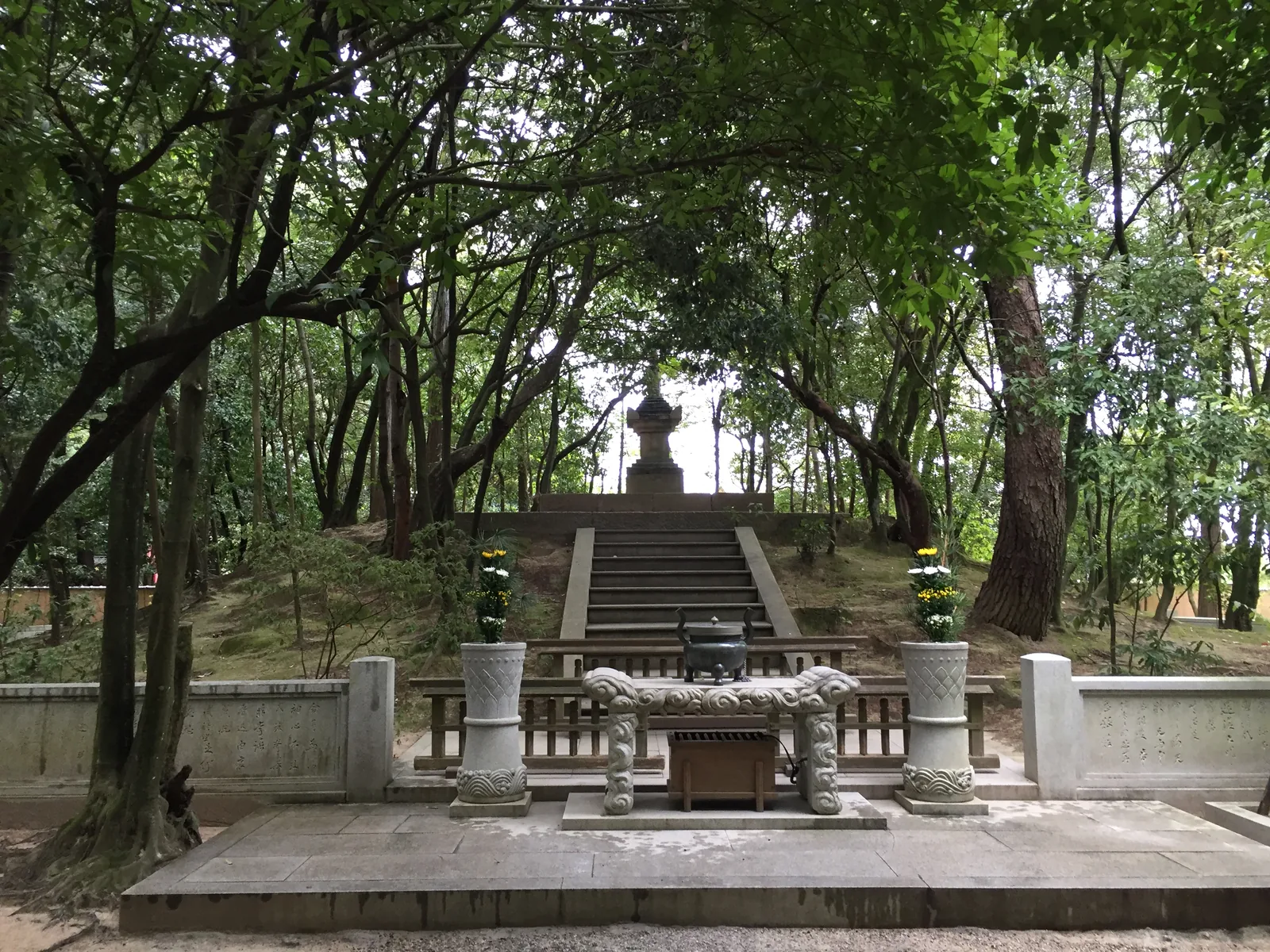 唐招提寺開山御廟：一段石階往上，盡頭是一座寶塔，階前圍著石造的矮柵與香爐，兩側供著菊花，四周是高大的杉與滿地的苔