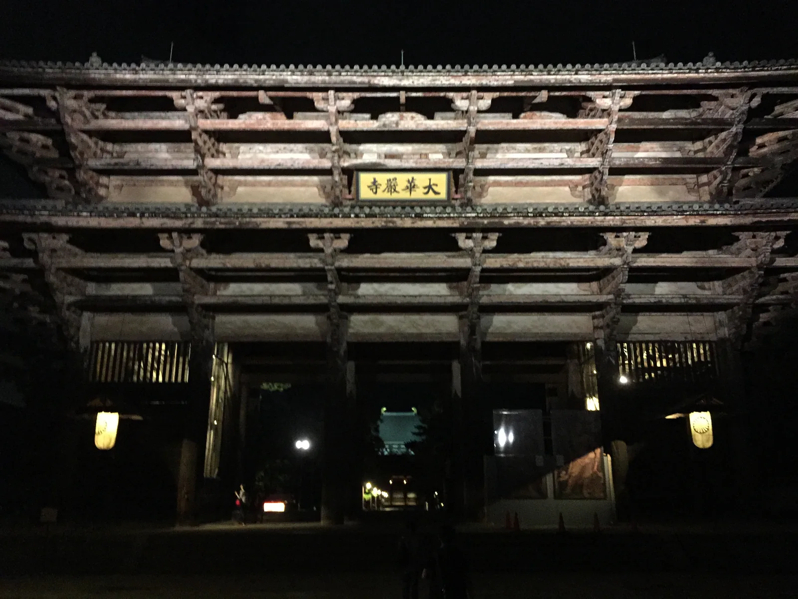 東大寺南大門的夜景：兩層的木造大門被投射燈打亮，上層正中掛著一塊金字扁額，寫著「大華嚴寺」；柱身上一層層向外挑出的橫材共六層，門下垂著兩盞點亮的燈籠