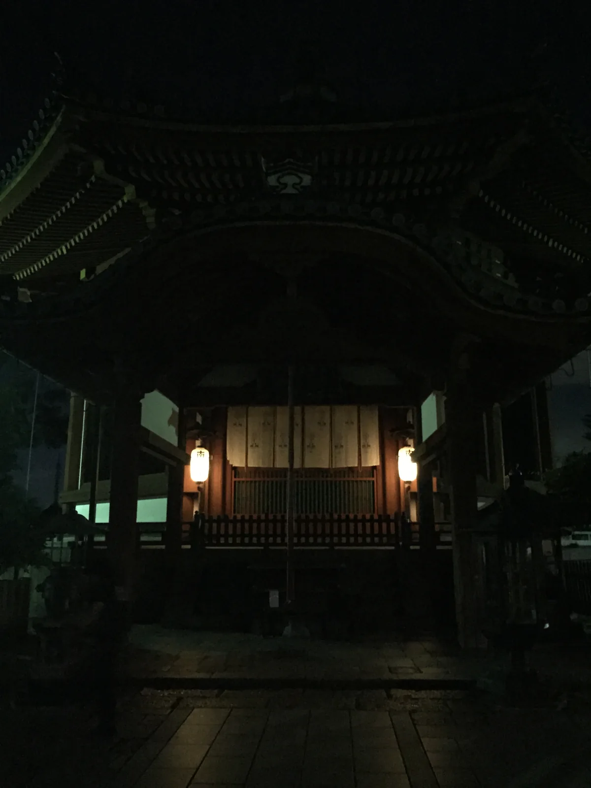 南圓堂正面：八角形的屋頂在夜裡只剩輪廓，正面伸出的拝所（はいしょ，供禮拜的前室）上加了一道唐破風（からはふ，中央拱高的曲線山牆），破風下的中備是雲形雕刻，兩根角柱之間掛著兩盞寫「南円堂」的提燈，扉關著
