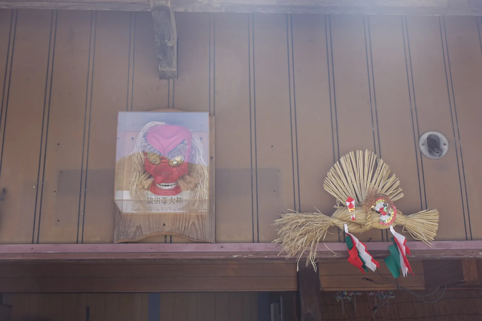 民家屋簷下並列的紅面神樂面與稻草注連飾