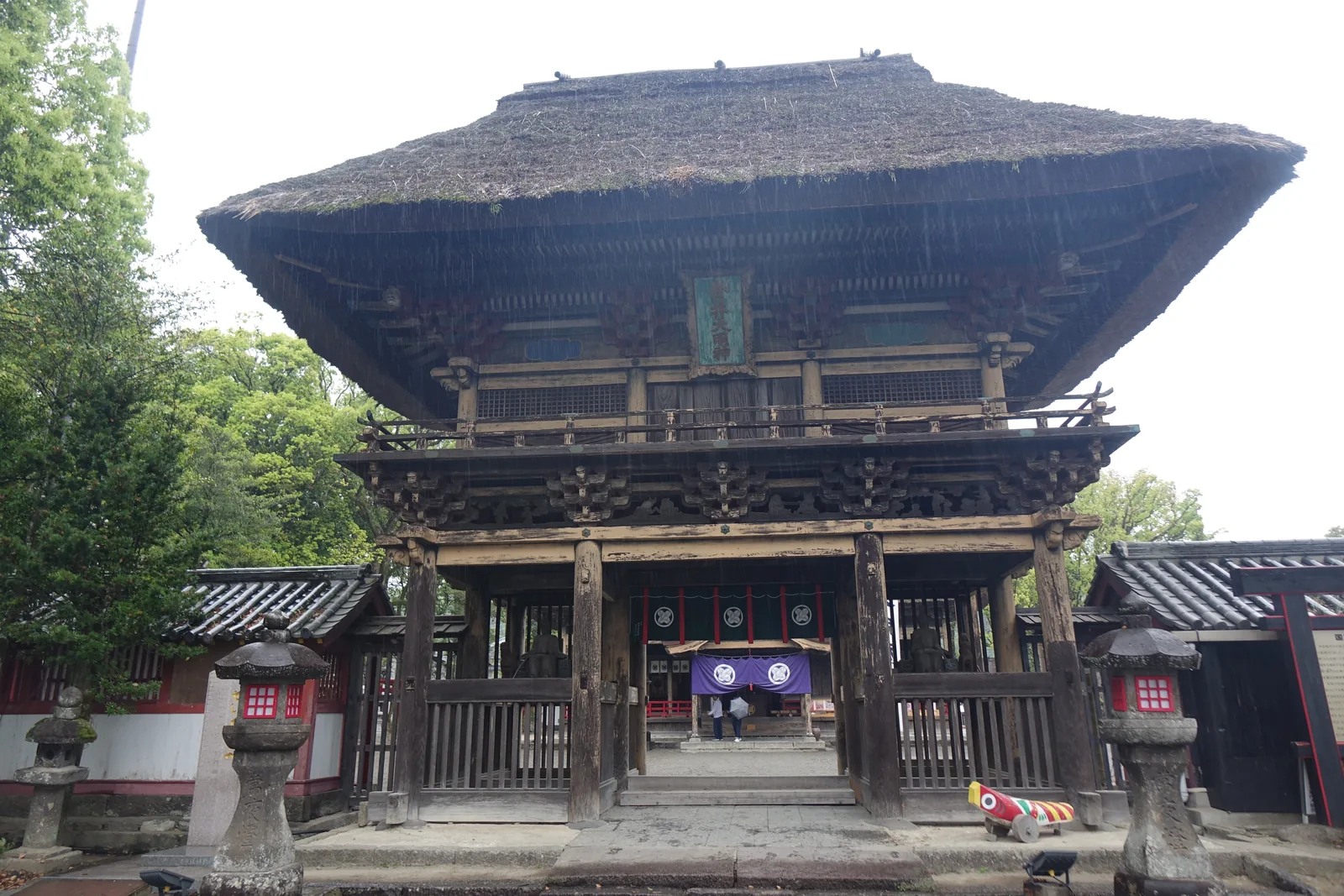 雨中的樓門正面，茅葺屋頂如小山隆起