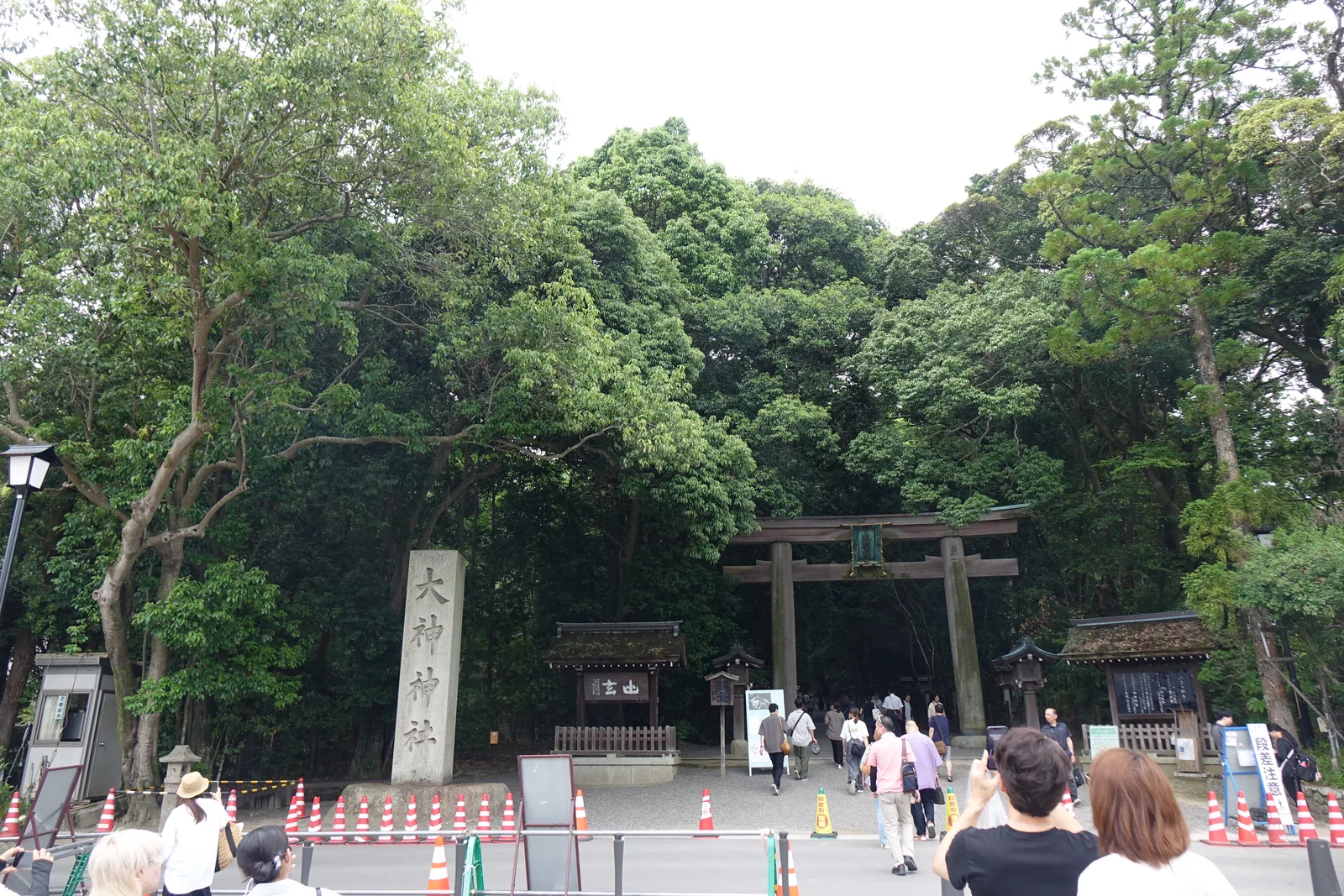 大神神社的二之鳥居遠景，素木的明神鳥居立在照葉樹林前，左側是高大的石造社號標